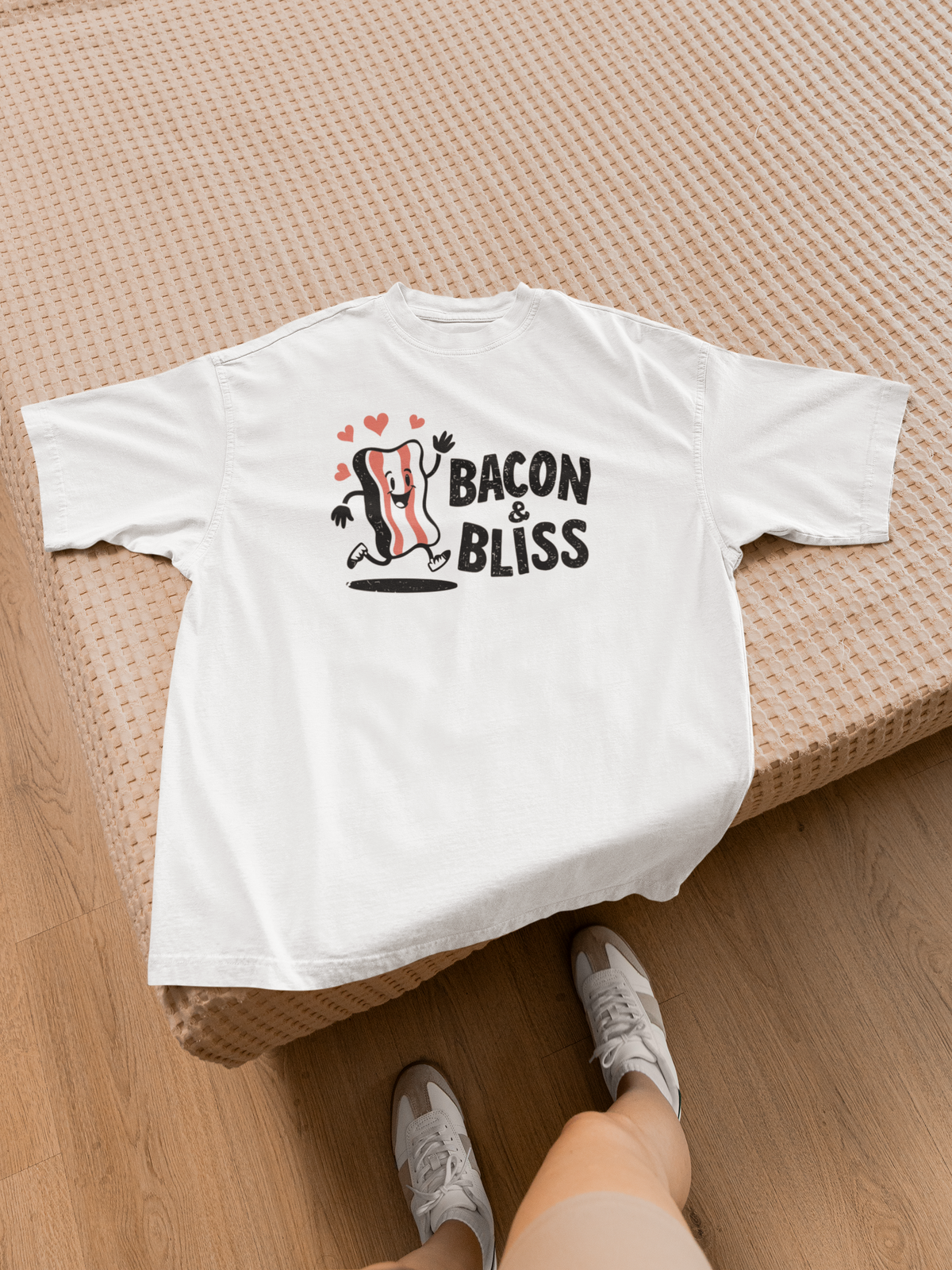 'Bacon & Bliss' t-shirt in white with bacon character print, laid on bed, funny bacon lover gift