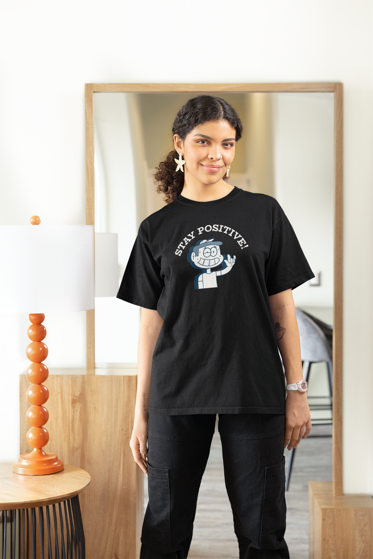 'Stay Positive!' t-shirt in black, woman wearing it in a stylish room, funny motivational graphic gift for her