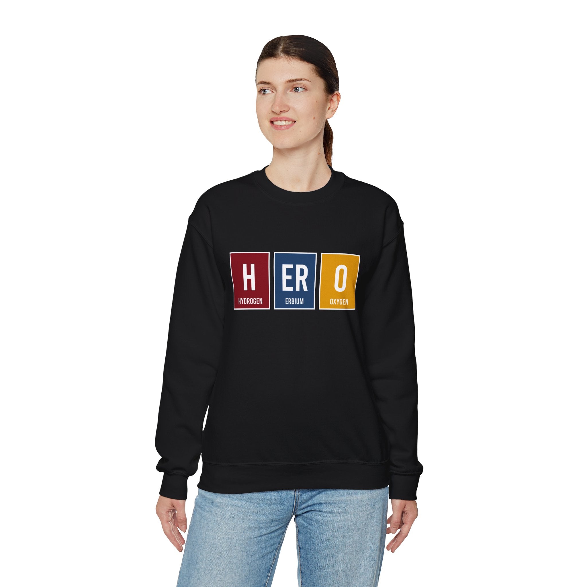 A person wearing a HERO - Sweatshirt, offering both comfort and style, with the word "HERO" spelled out using periodic table elements, stands against a plain white background. Perfect for staying warm during winter.