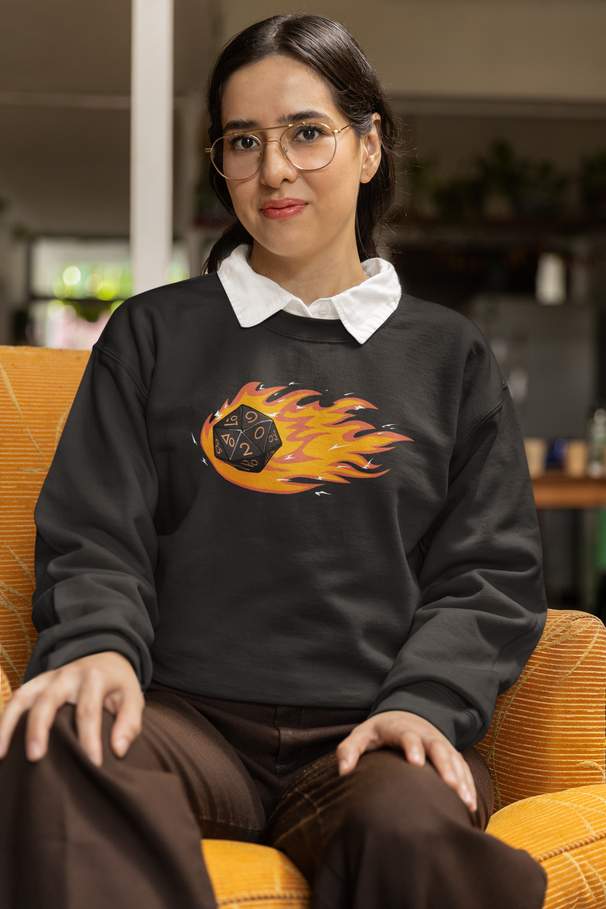 "Polyhedral Dice On Fire" sweatshirt in charcoal, woman sitting indoors wearing glasses, funny gift