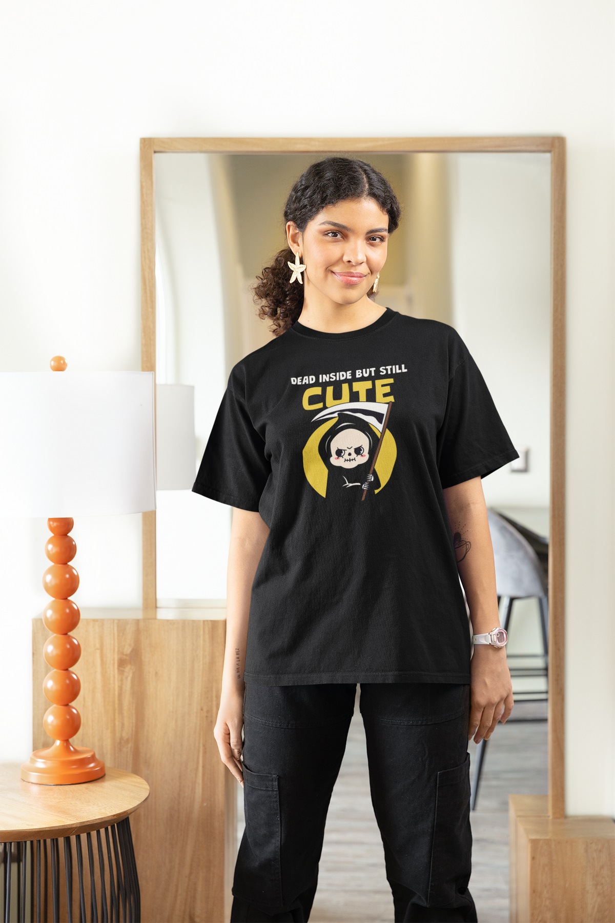 'Dead Inside but Still Cute' t-shirt in black, woman wearing it in a stylish room, funny goth pun graphic gift