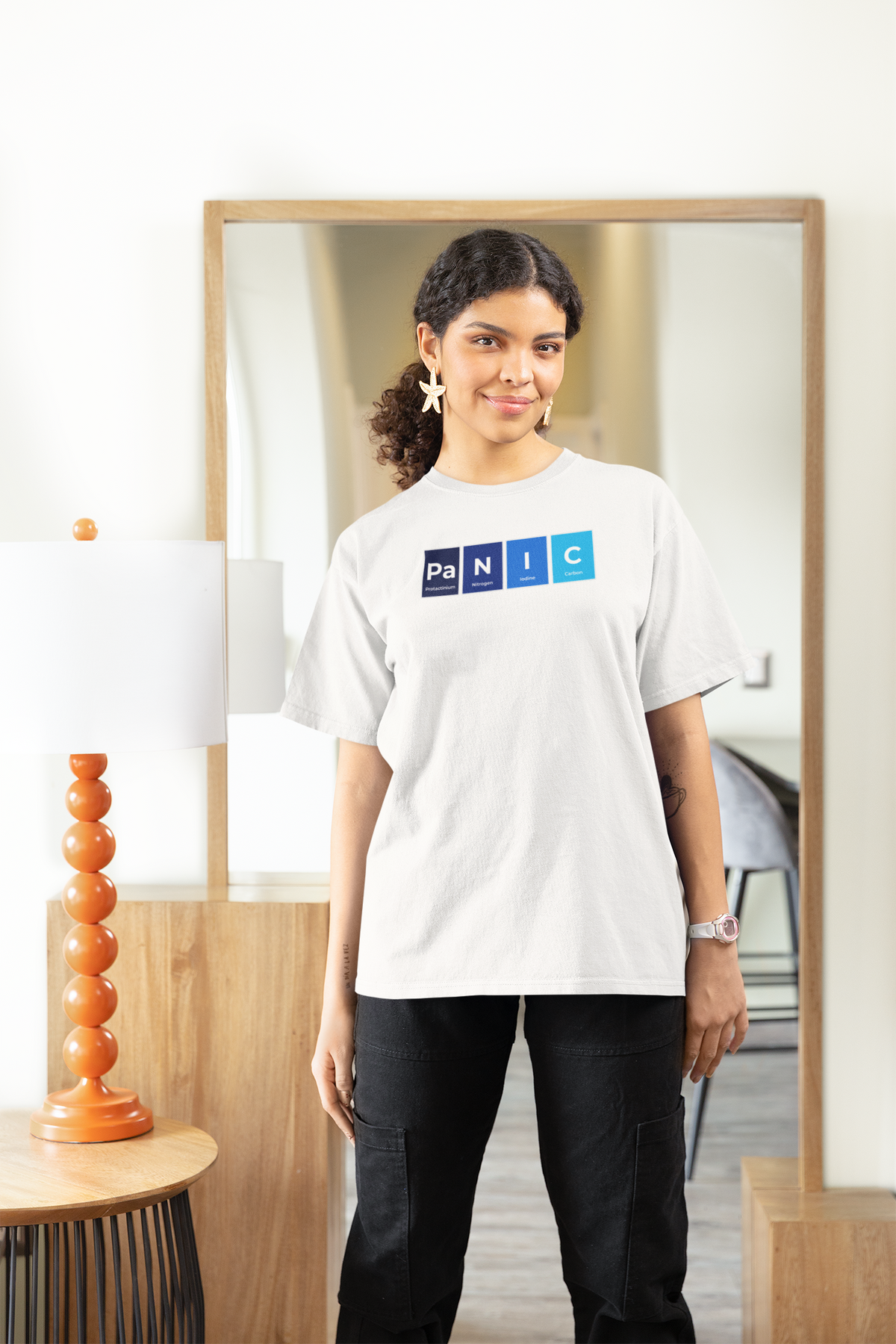 'Pa-N-I-C' periodic table women's tee in white, woman standing at home, casual lifestyle photo