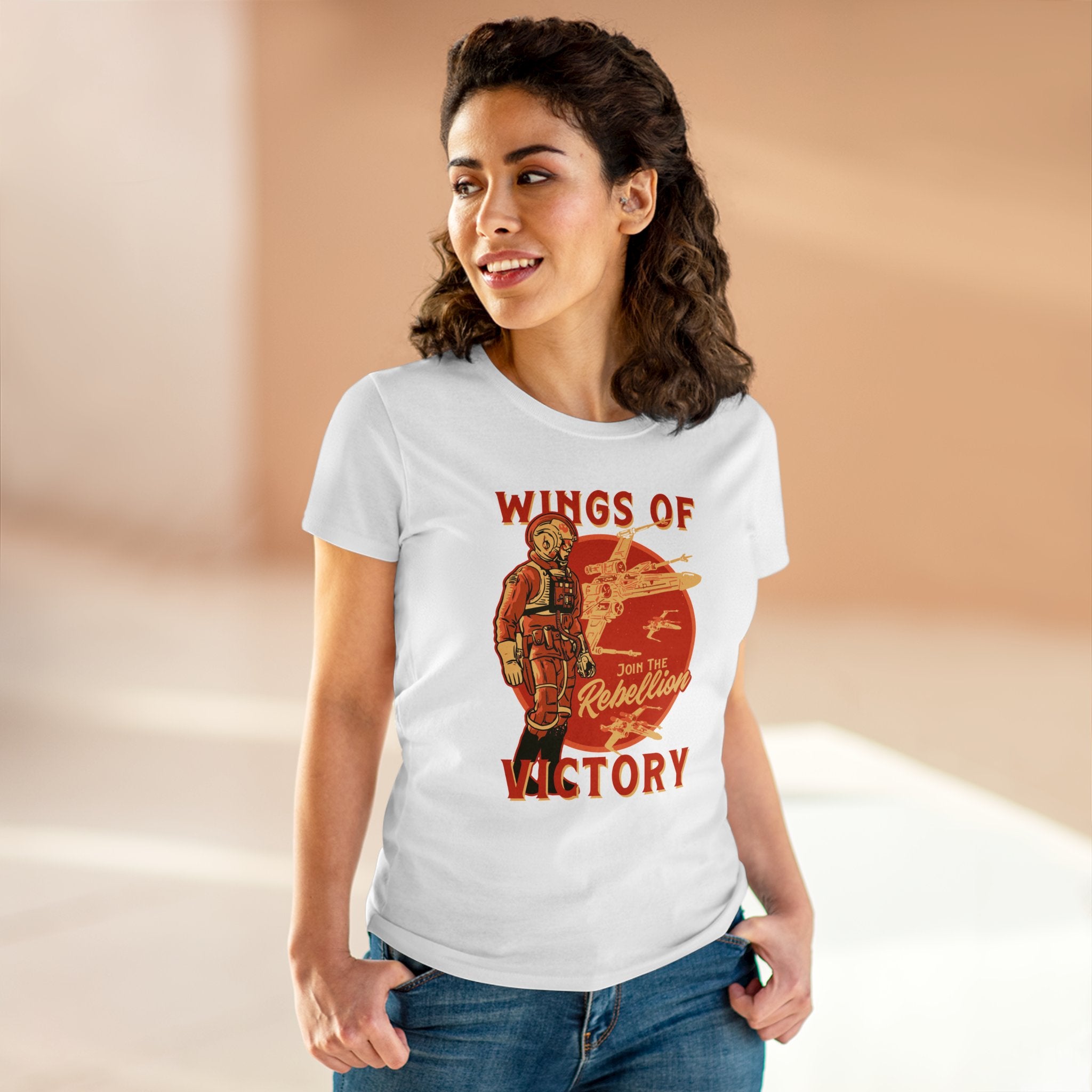 A woman with curly hair stands in a casual setting, wearing a pre-shrunk Wings of Victory - Women's Tee featuring a graphic of a pilot and the text "Wings of Victory - Join the Rebellion.
