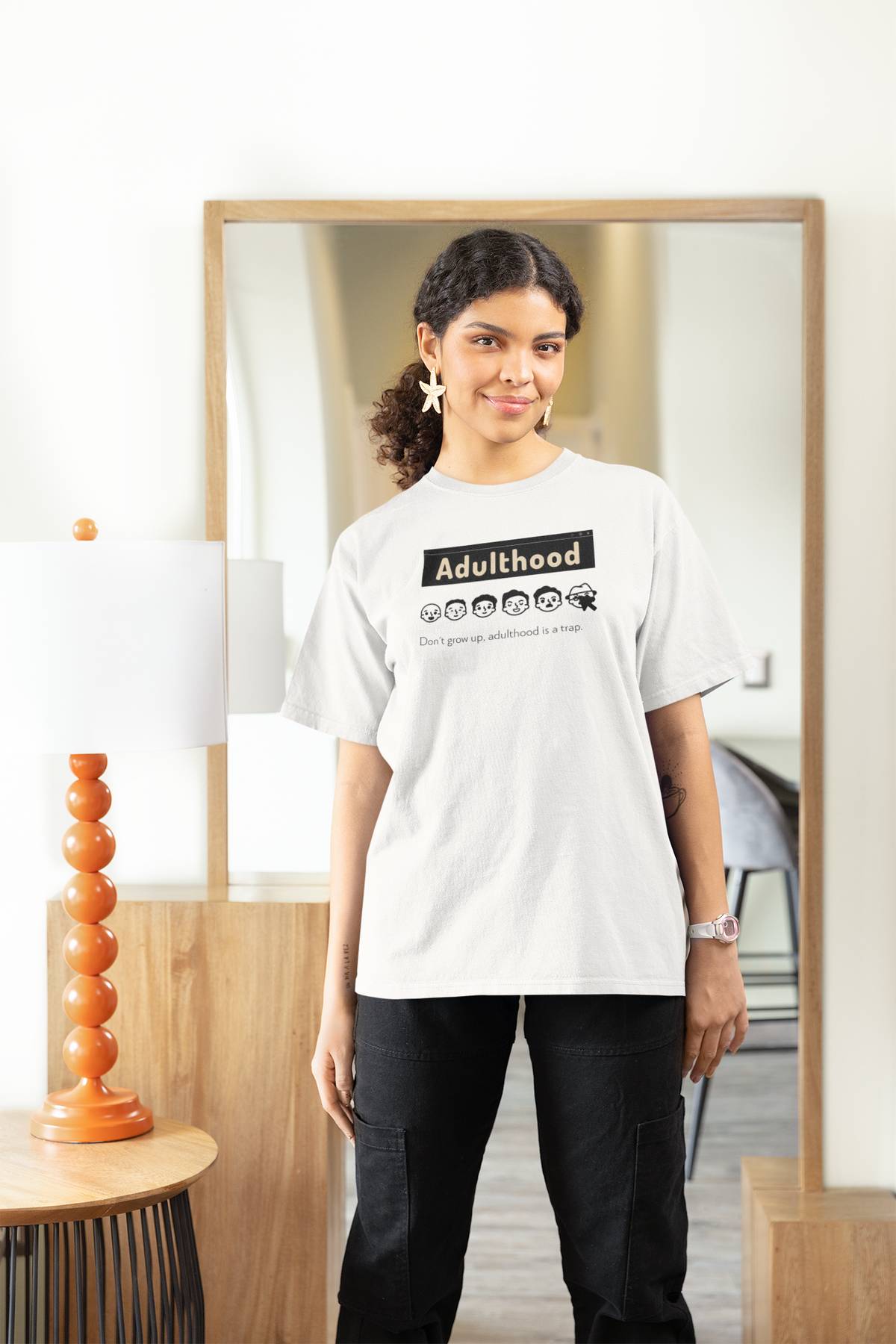 'Adulthood is a Trap' women's tee in white, woman wearing it at home, funny sarcastic shirt gift