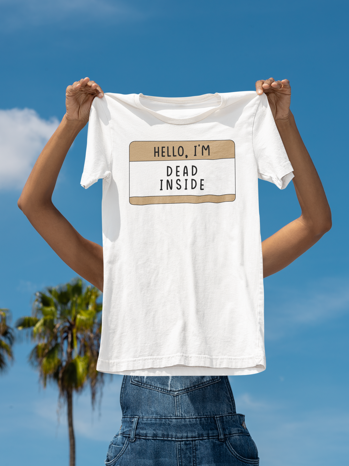 Hello I'm Dead Inside name tag T-shirt in white, man holding it up against sky backdrop, sarcastic tee