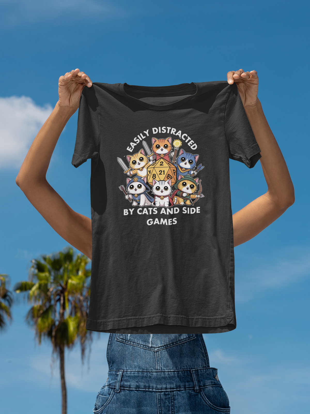 'Easily Distracted By Cats And Side Games' tee held up by man on beach with palm trees, cat lover gift