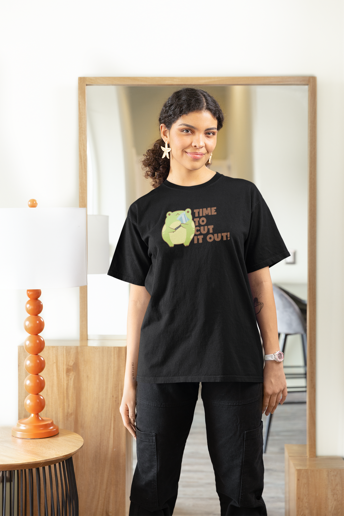 'Time to Cut It Out' frog women's tee in black, woman wearing it at home, funny science pun gift