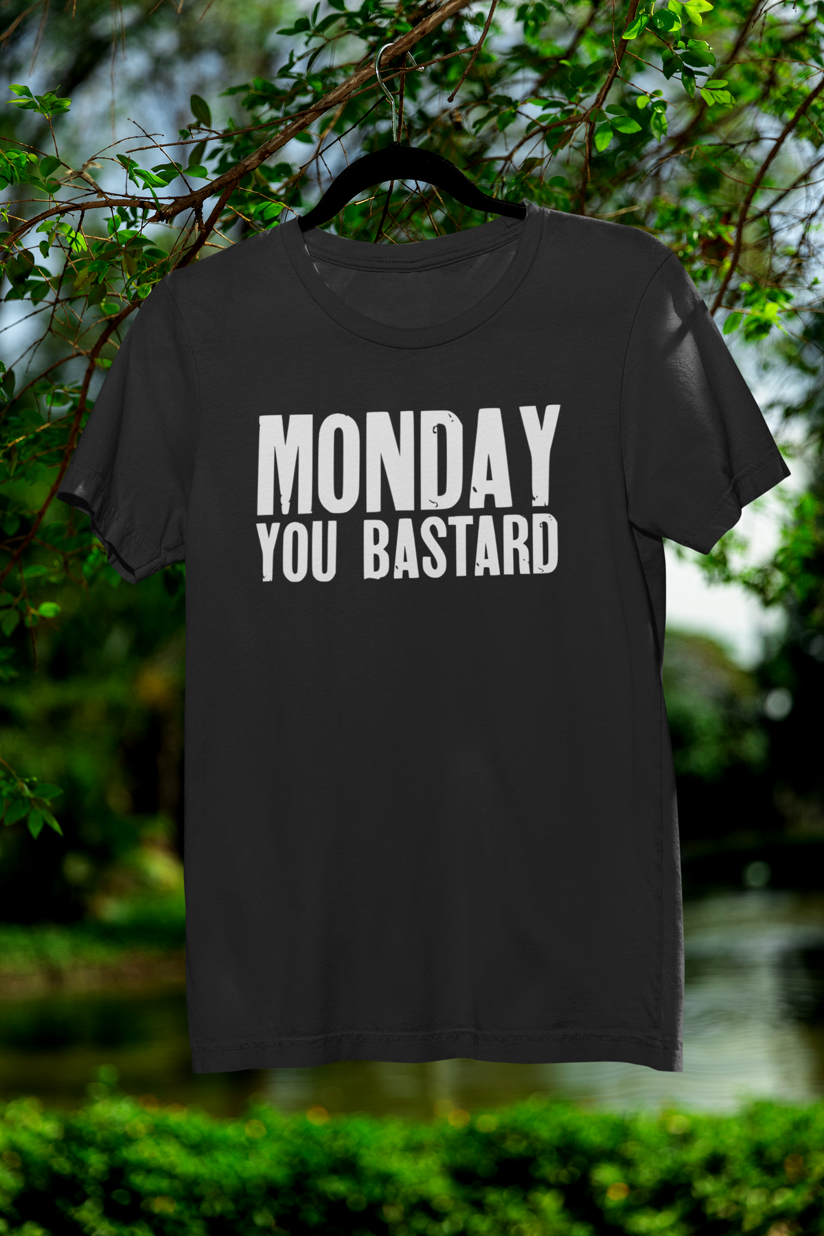 'Monday You Bastard' t-shirt in black, hanging outdoors among trees, funny anti-Monday humor gift