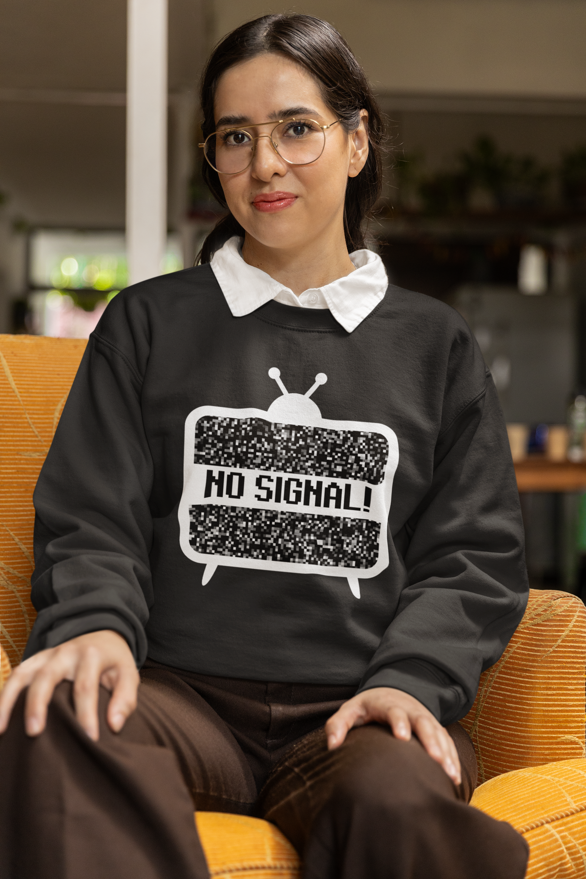 'No Signal' crewneck sweatshirt in charcoal grey, woman sitting in chair wearing it, cozy retro TV gift