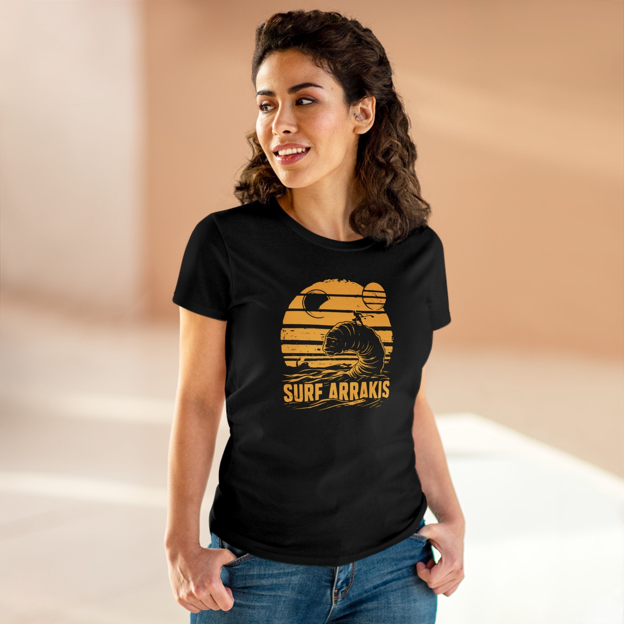 Woman wearing a Surf Arrakis - Women's Tee made of soft light cotton with a pre-shrunk comfy design. She is standing indoors, looking to the side, and has her hands in her pockets.