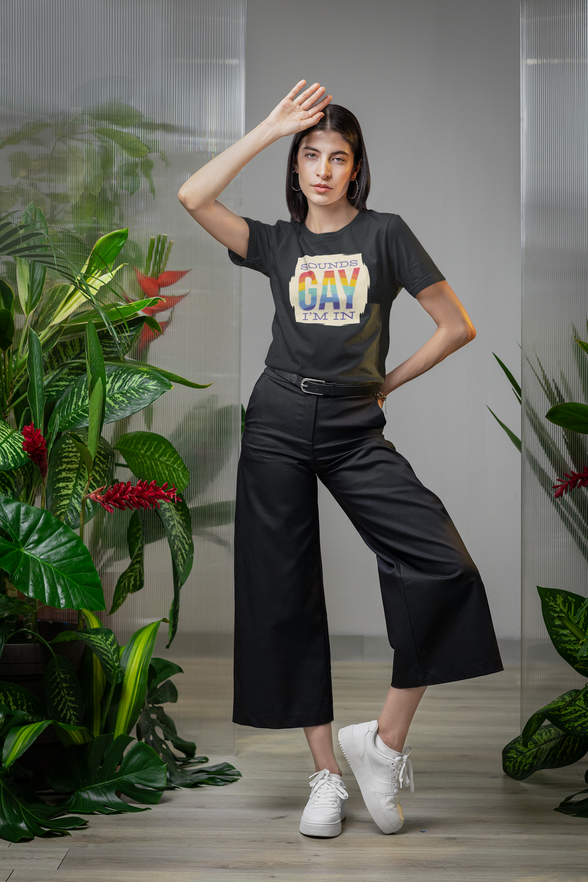 'Sounds Gay I'm In' T-shirt in black, woman wearing it in a plant-filled setting, pride gift shirt