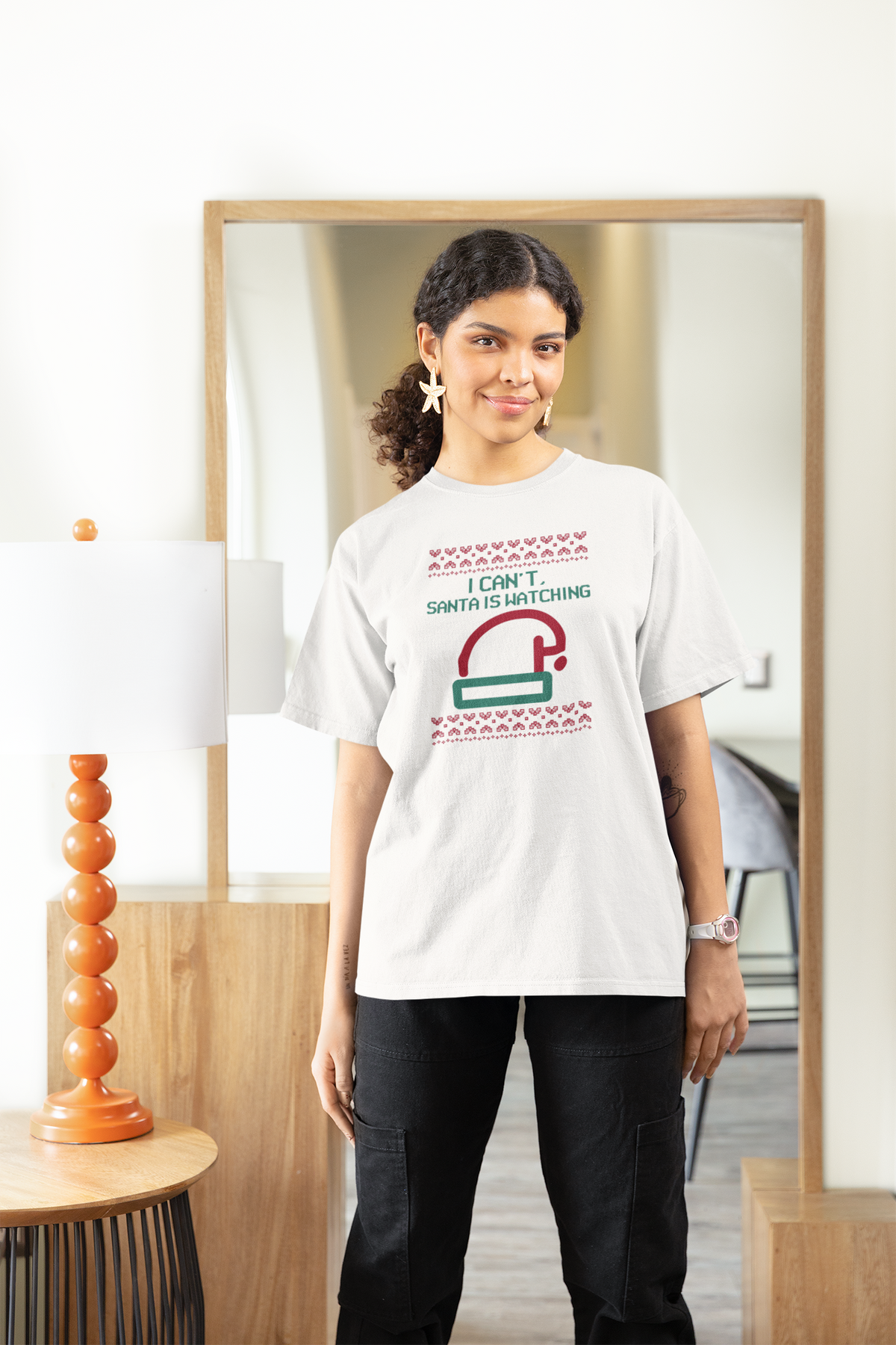 'I Can't Santa Is Watching' camera graphic tee in white, woman wearing it at home, funny Christmas t-shirt gift