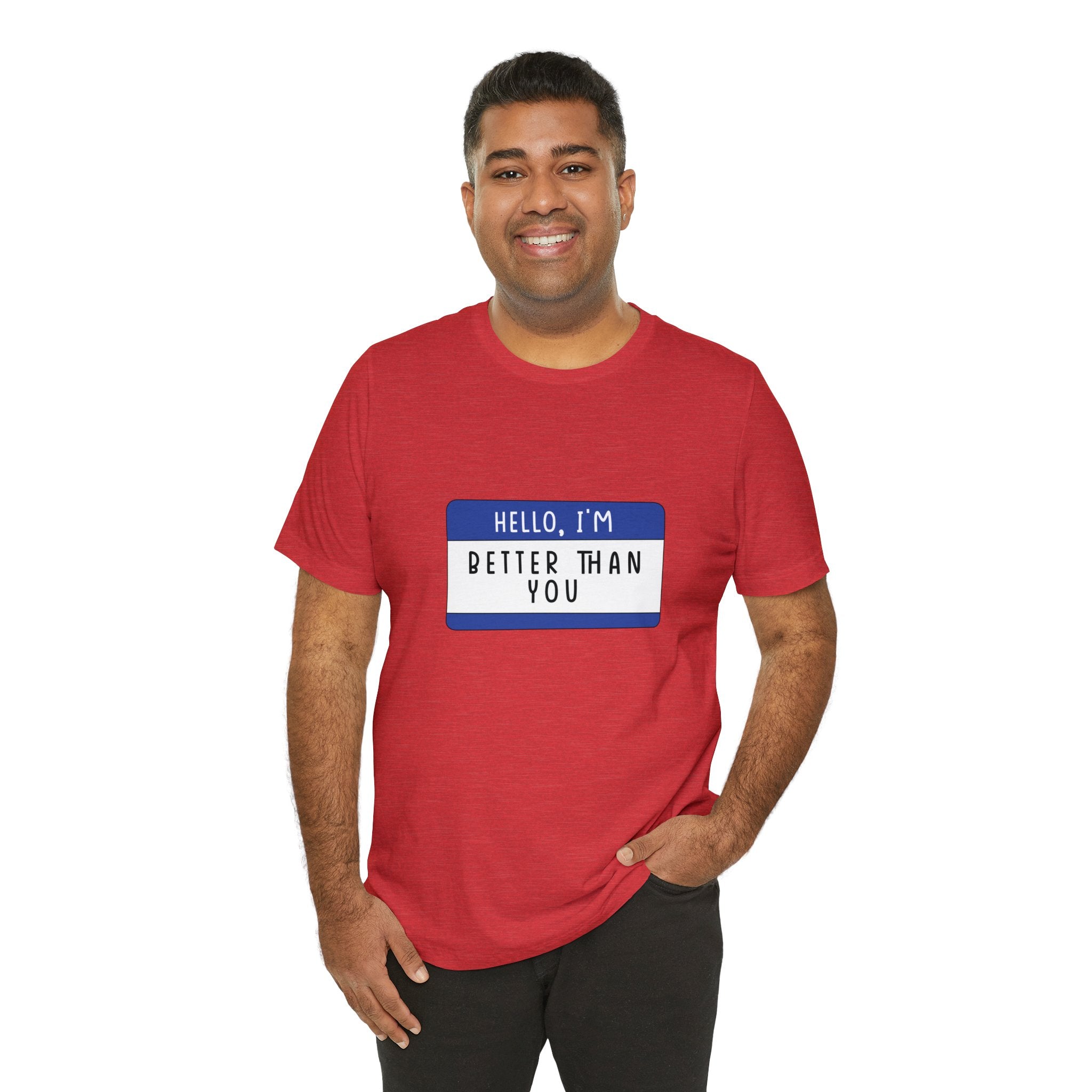 A man smiling in a red "Hello, I'm Better Than You" t-shirt with geeky charm and a blue name tag that reads "hello, I'm better than you." He stands against a white background.