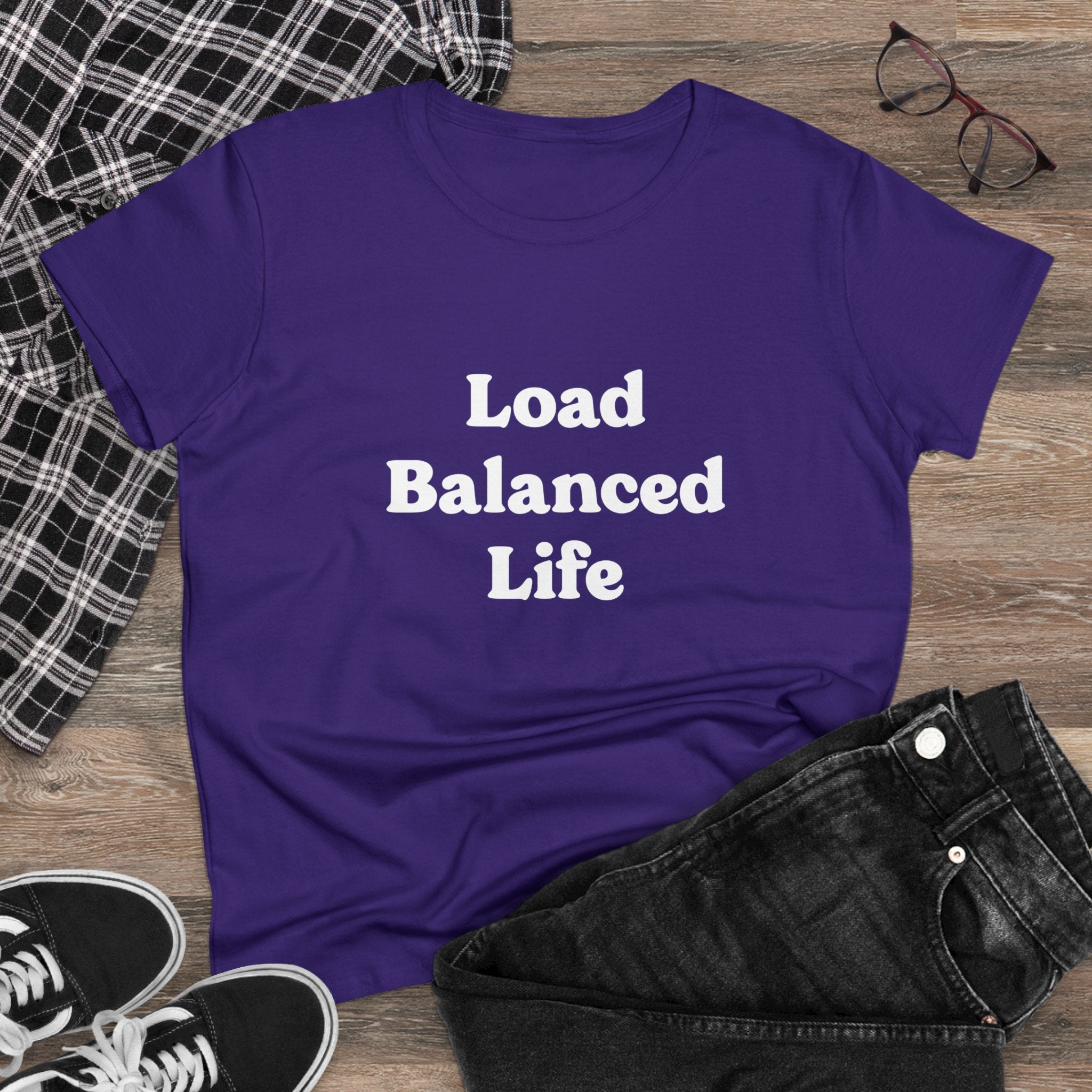 The Load Balanced Life - Women's Tee in purple, featuring the "Load Balanced Life" text, is made from pre-shrunk cotton for a stylish and comfortable fit. Displayed on a wooden surface, it is combined with a plaid shirt, jeans, glasses, and sneakers to create an ideal casual look.