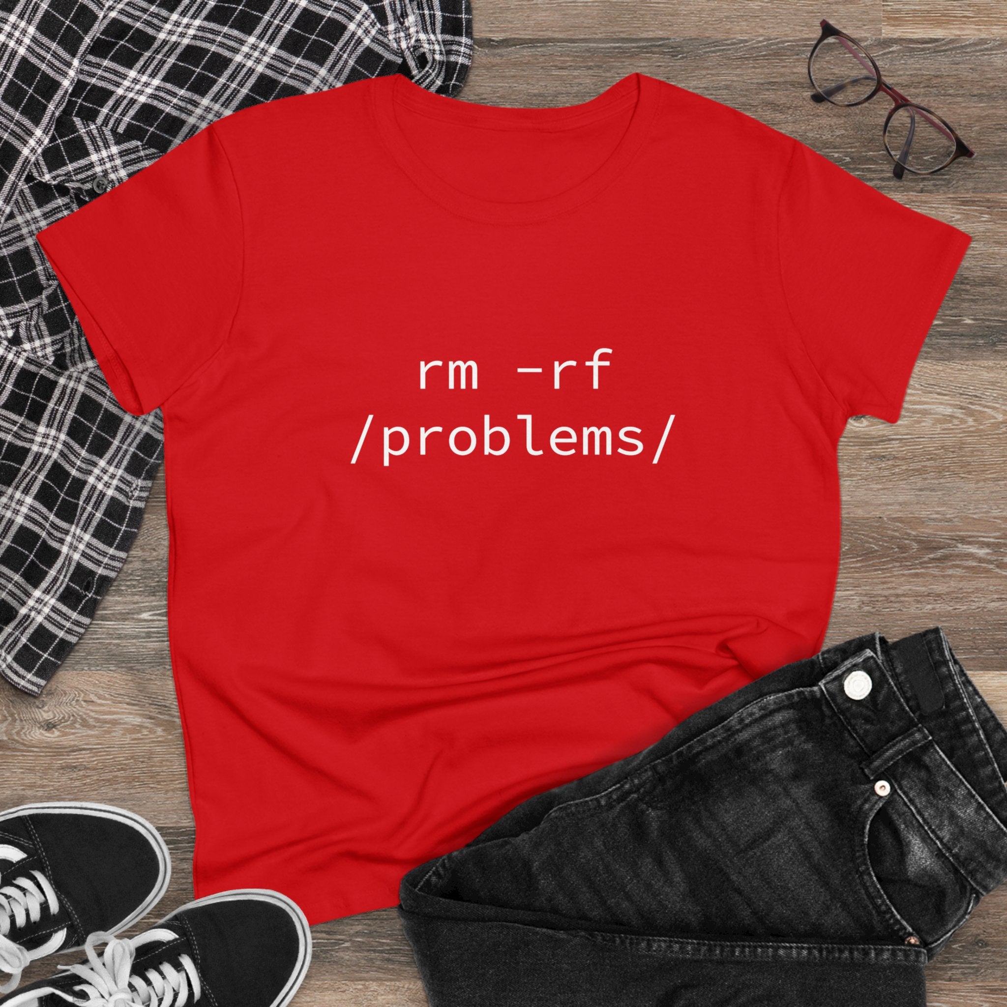 The RMRF Problems - Women's Tee, made from pre-shrunk cotton and featuring the striking "rm -rf /problems/" design, is styled alongside a plaid shirt, black jeans, glasses, and sneakers on a wooden floor. Perfect for anyone looking to make a statement.