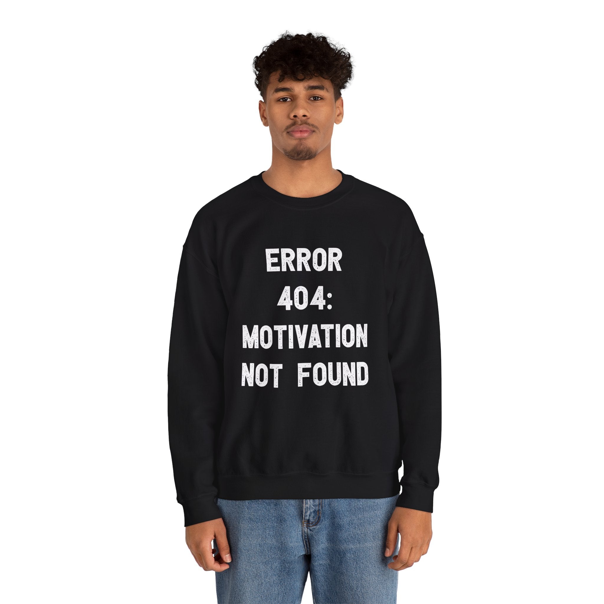 A person stands facing forward, wrapped in the cozy comfort of a black Error 404: Motivation not found - Sweatshirt with white text reading, "ERROR 404: MOTIVATION NOT FOUND." They have short curly hair and are wearing light blue jeans—perfect attire for the colder months.