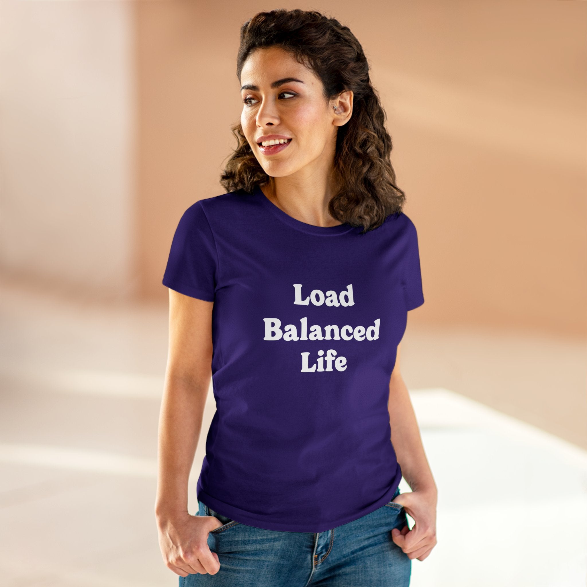 A person wearing the stylish and comfortable "Load Balanced Life - Women's Tee" in purple, crafted from pre-shrunk cotton, stands in a softly lit room.