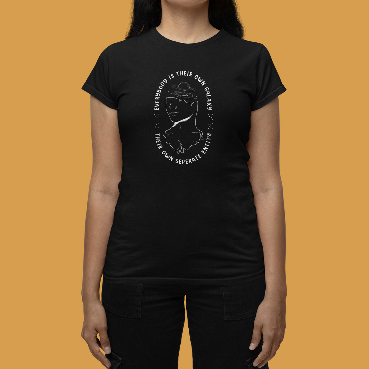 'Everybody Is Their Own Galaxy' illustrated women's t-shirt in black, close-up on model, orange backdrop, gift