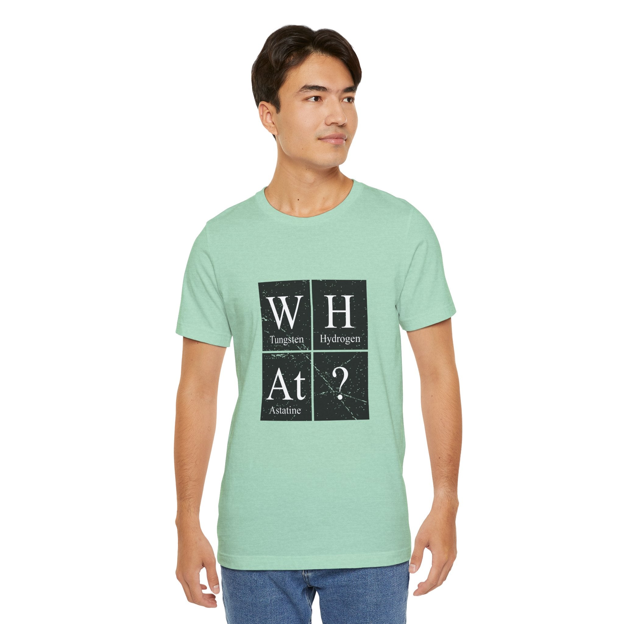 Young man wearing a light green unisex jersey tee with the W-H-At-? design featuring the elements tungsten (W), hydrogen (H), and astatine (At) with a question mark.