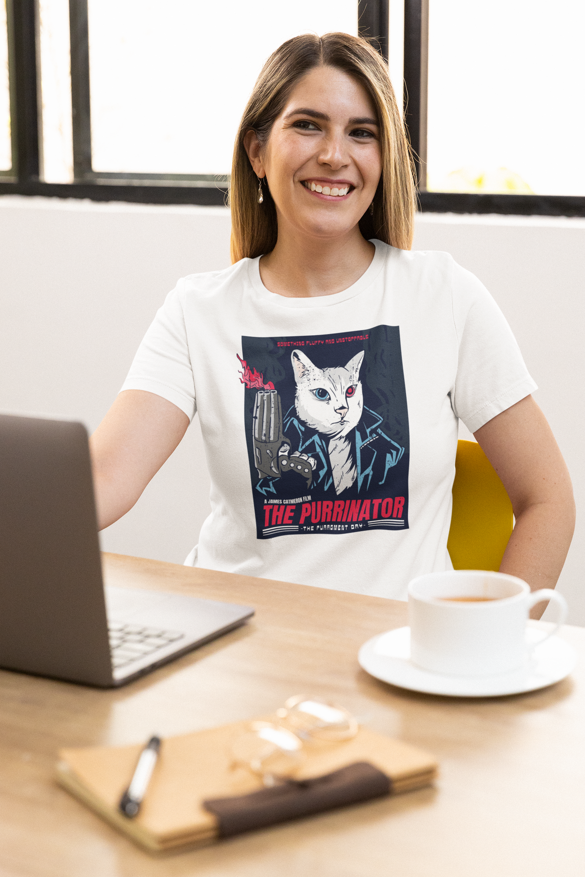 'The Purrinator' t-shirt in white, woman model wearing it at a desk with a laptop, funny gift for cat lovers