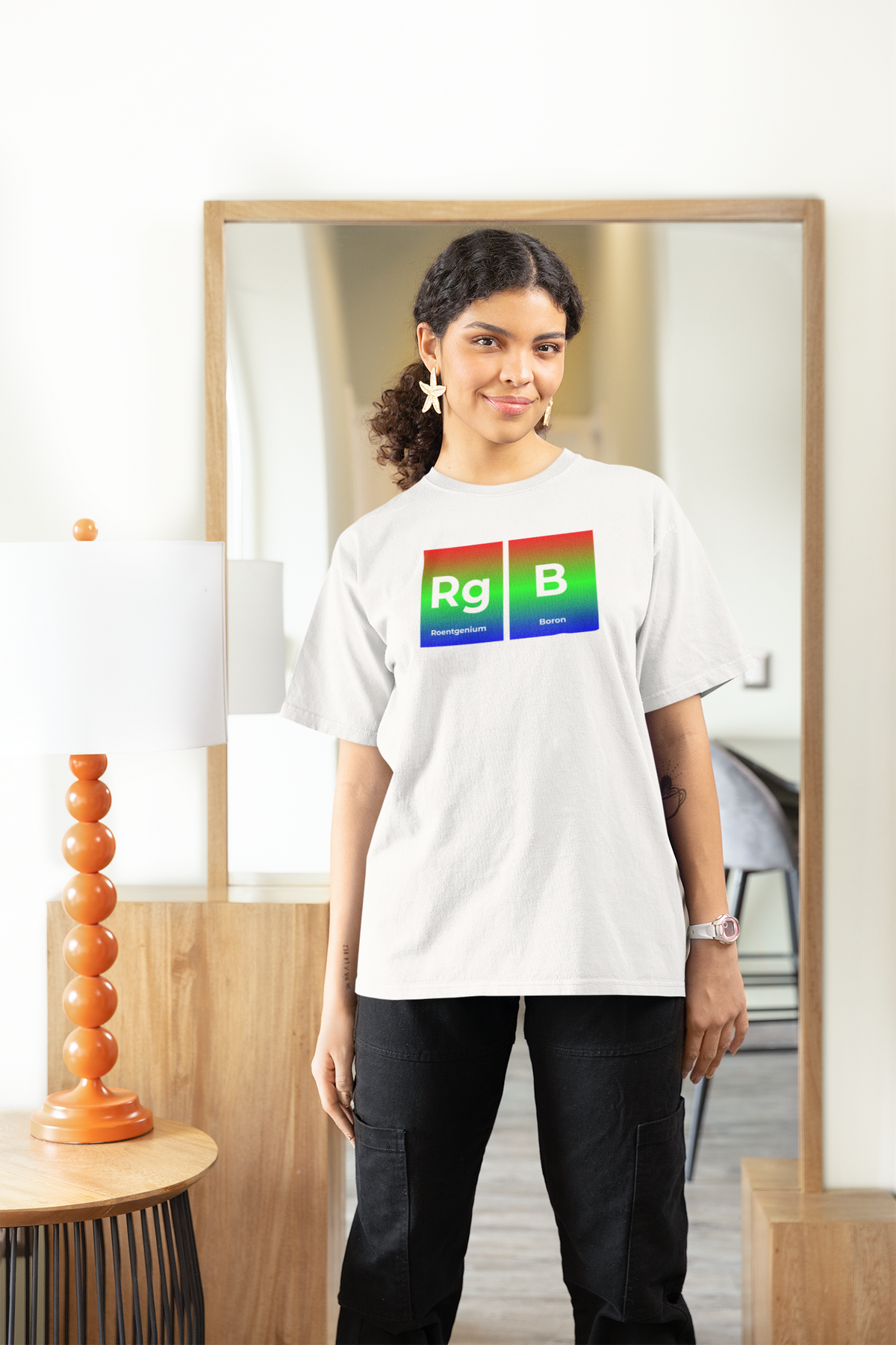 'RG-B' periodic table women's tee in white, woman standing at home, casual lifestyle photo