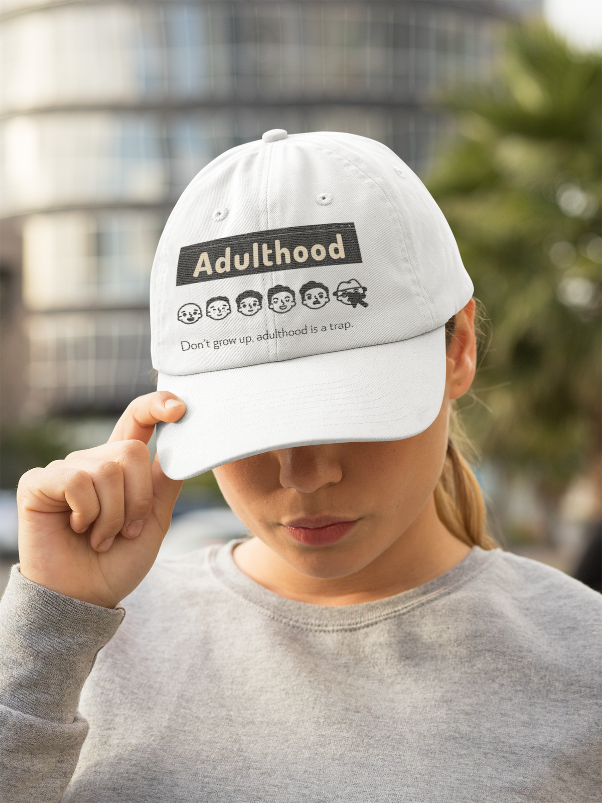 'Adulthood is a Trap' dad hat in white, woman wearing it outdoors, funny sarcastic hat gift idea