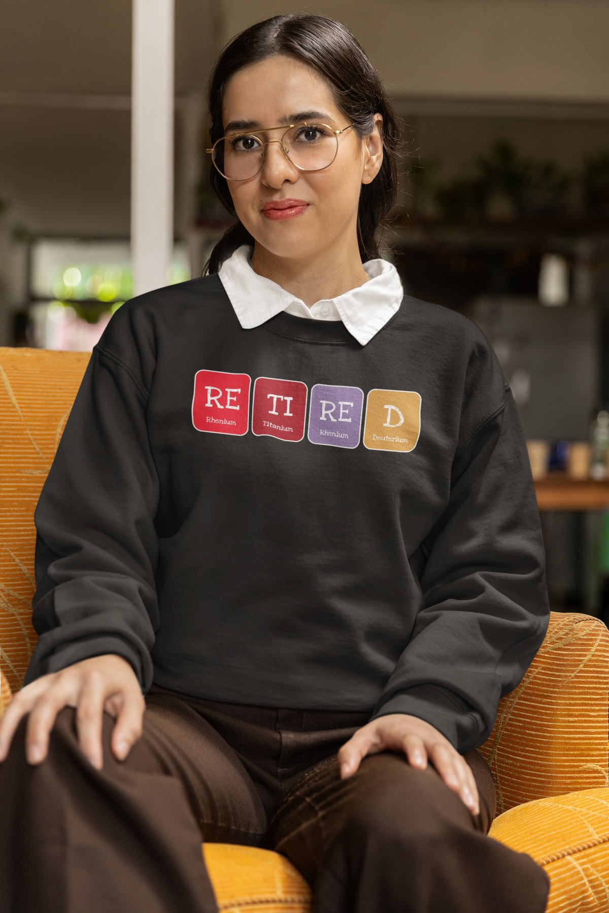 'Retired' periodic table sweatshirt in charcoal, woman sitting in an armchair wearing it, cozy photo