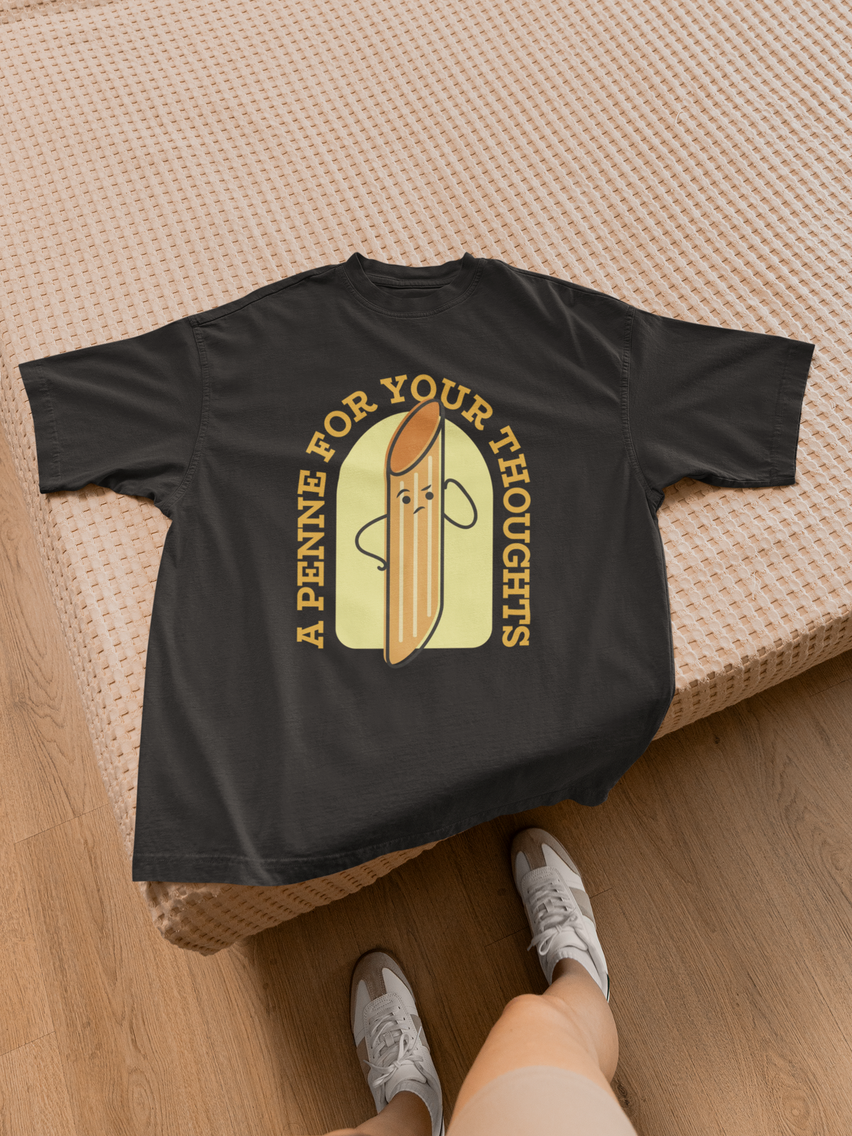 'A Penne For Your Thoughts' pasta t-shirt in black, flat lay on a bed