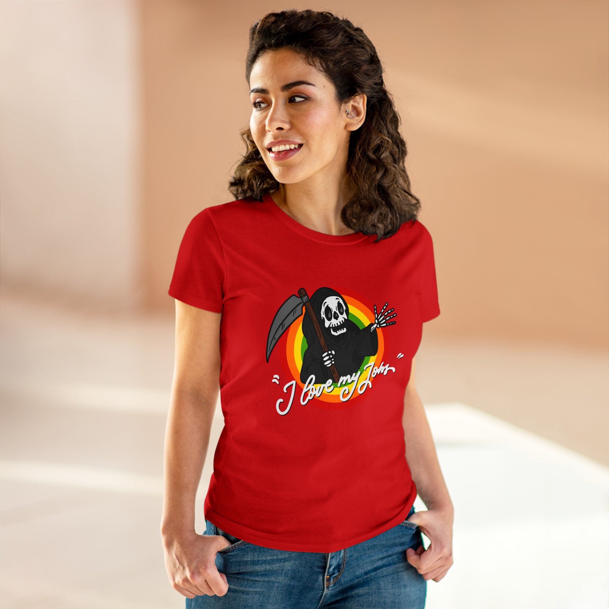 A person is wearing a red T-shirt featuring a cartoon skeleton with a scythe and the text "I love my job." This Love My Jobs - Women's Tee is made from soft, comfortable cotton. The background is blurred and features warm tones.