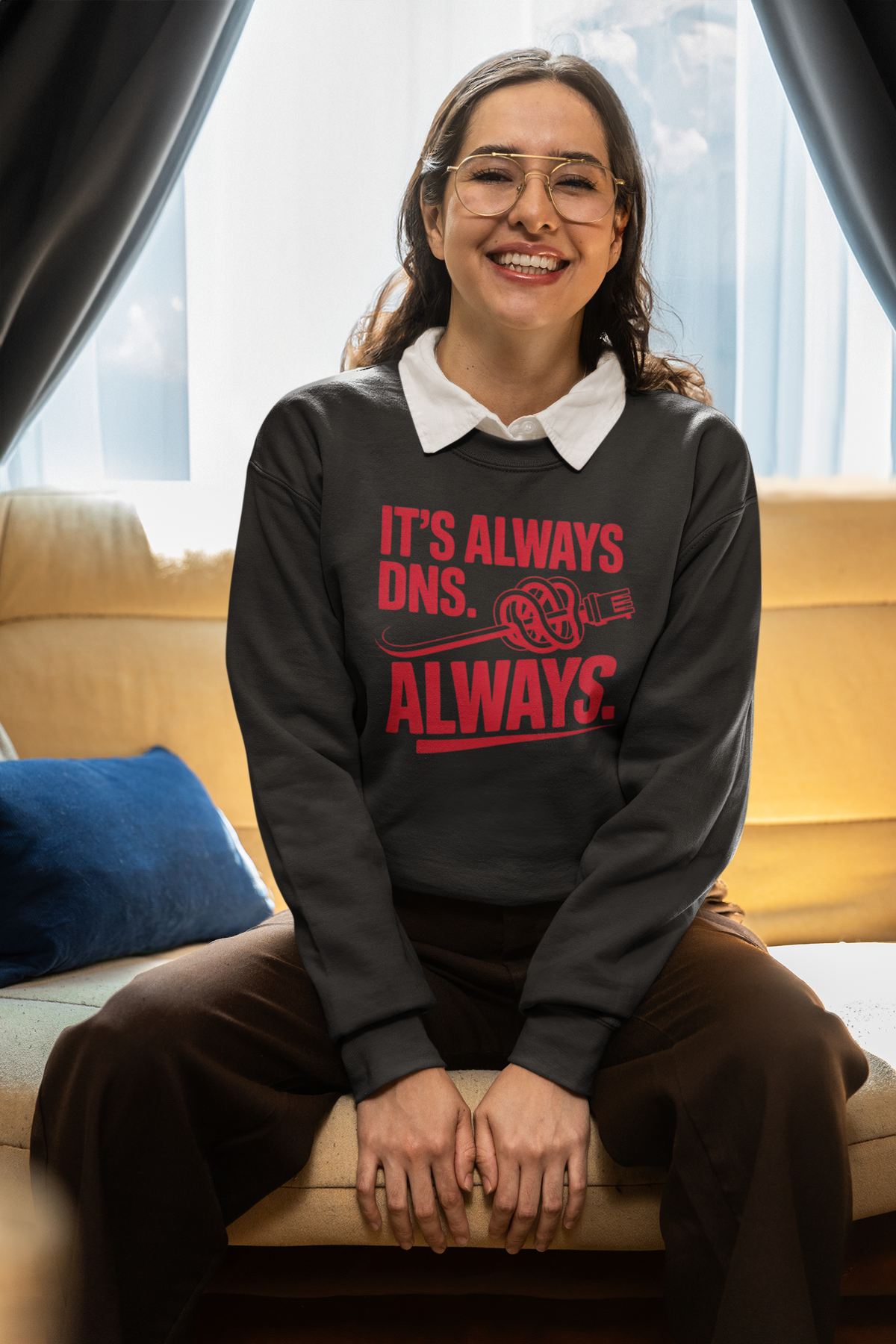 'It's Always DNS. Always.' black sweatshirt worn by woman sitting indoors, funny sysadmin gift