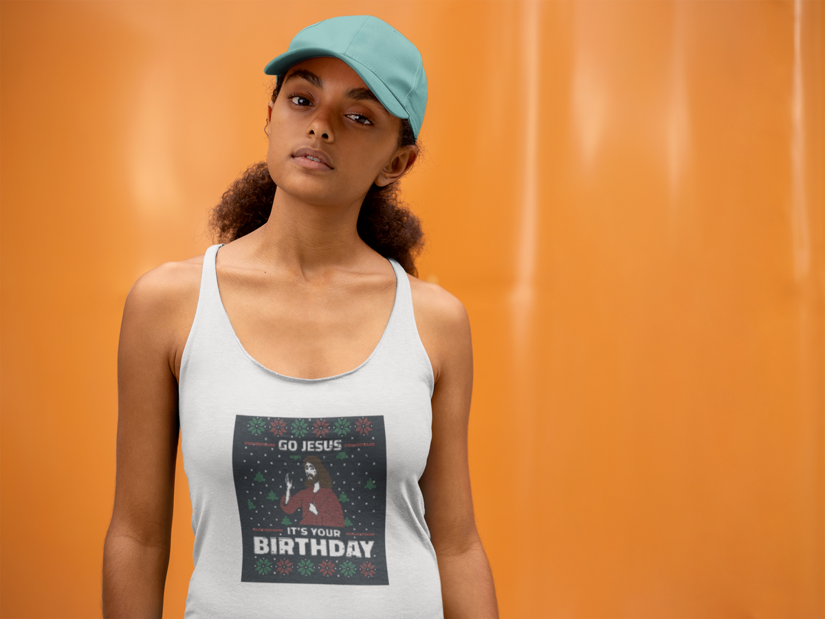 'Go Jesus It's Your Birthday' racerback tank top in white, woman wearing it by an orange wall, Tank Top mockup, Geekpsters