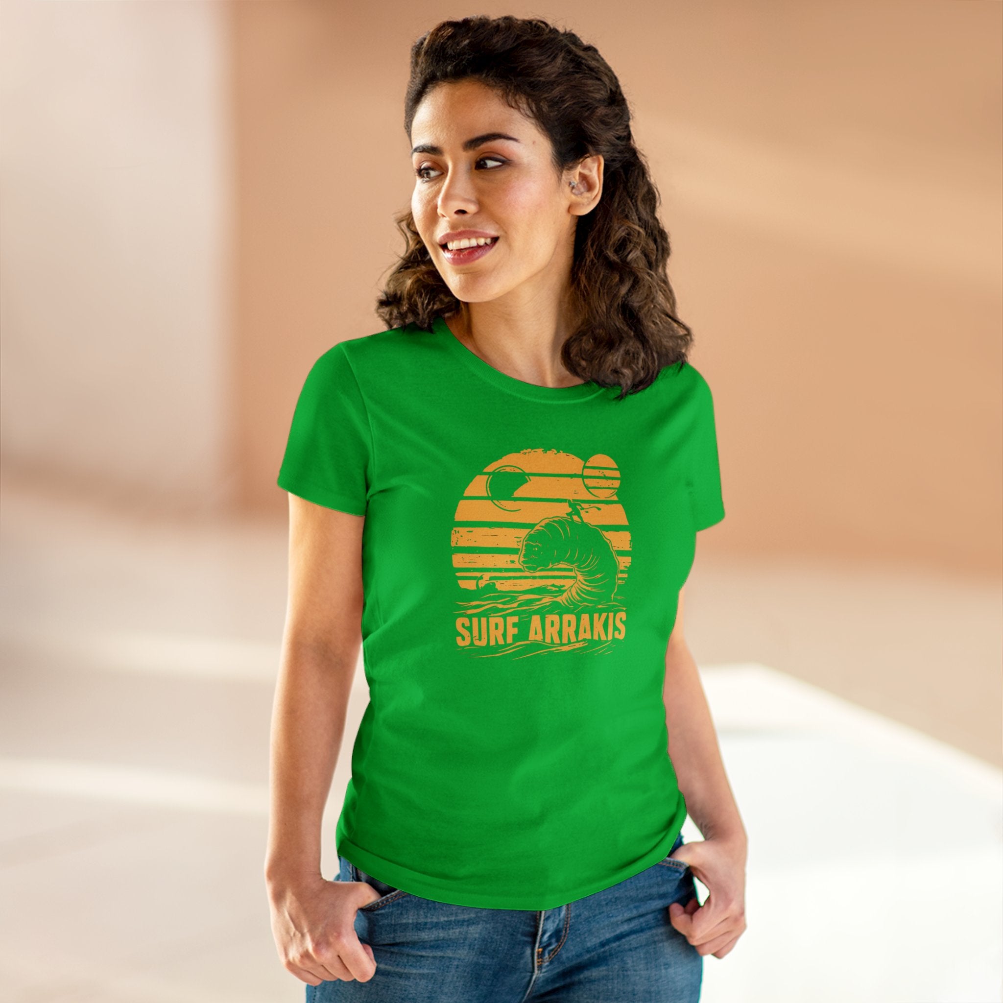 A woman wearing a green Surf Arrakis - Women's Tee, crafted from soft light cotton with a comfy design, stands indoors and smiles while looking to the side.