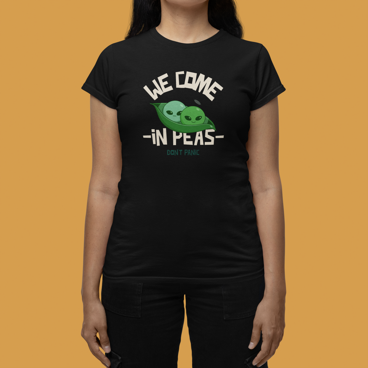 'We Come in Peas' t-shirt in black, woman wearing it in a stylish room, funny sci-fi pun tee gift