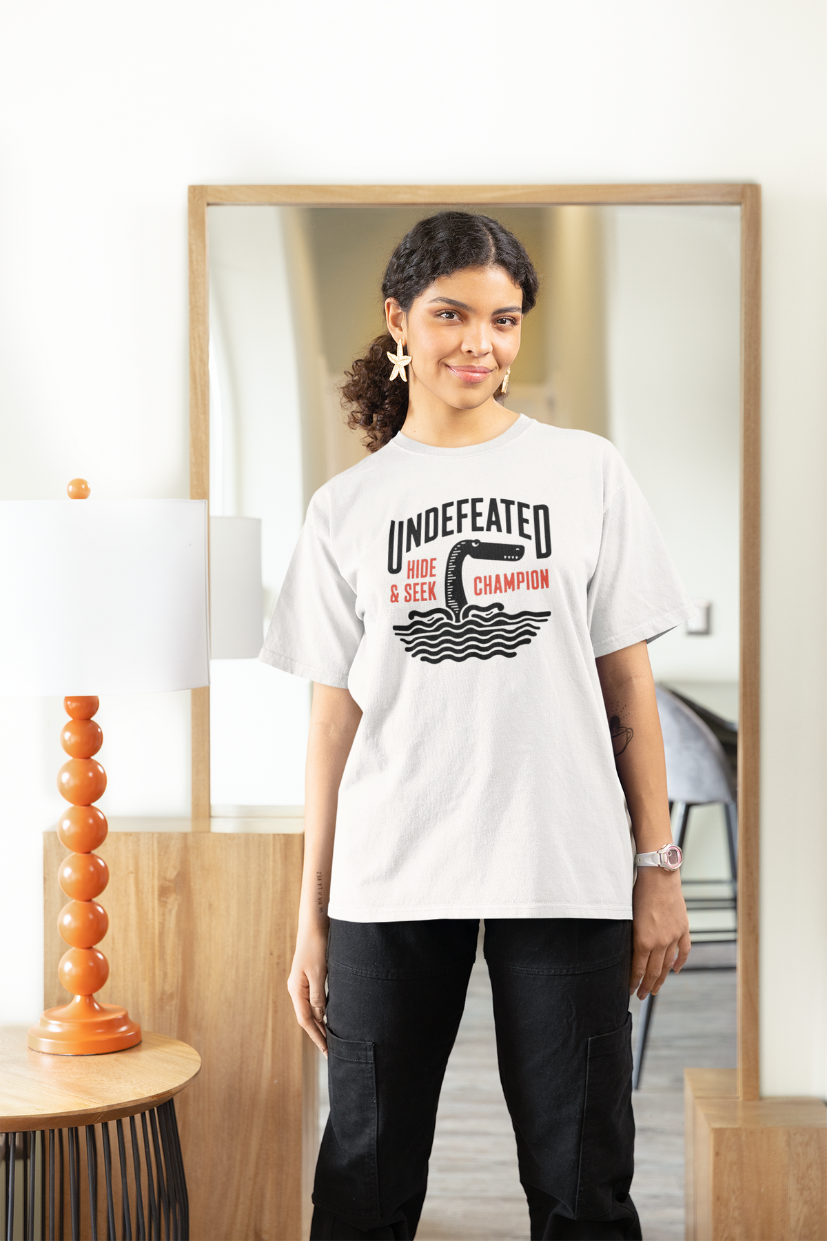 "Undefeated Hide and Seek Champion" women's tee in white, woman modeling it at home, funny game gift