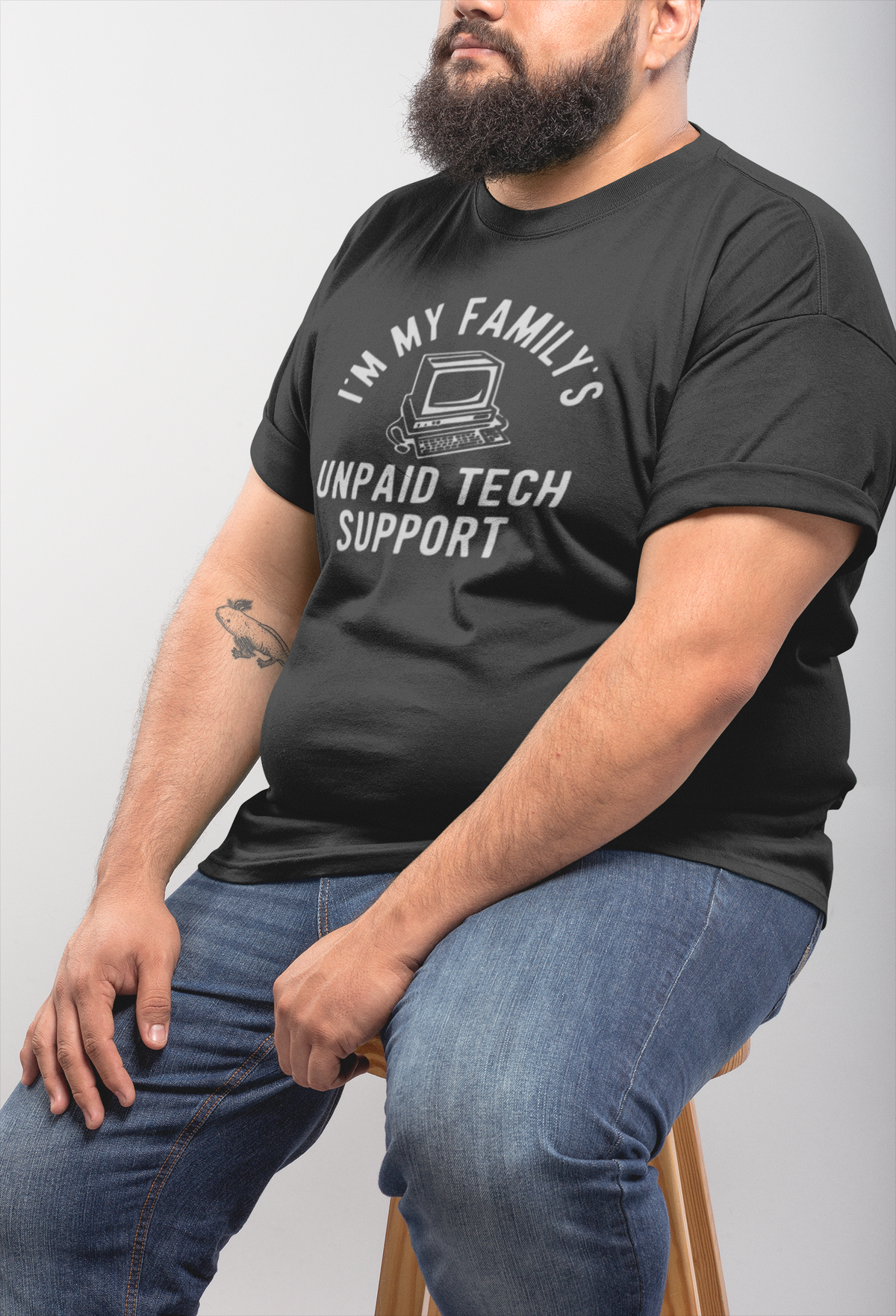 I'm My Family's Unpaid Tech Support charcoal t-shirt worn by a bearded man sitting sideways, funny IT gift