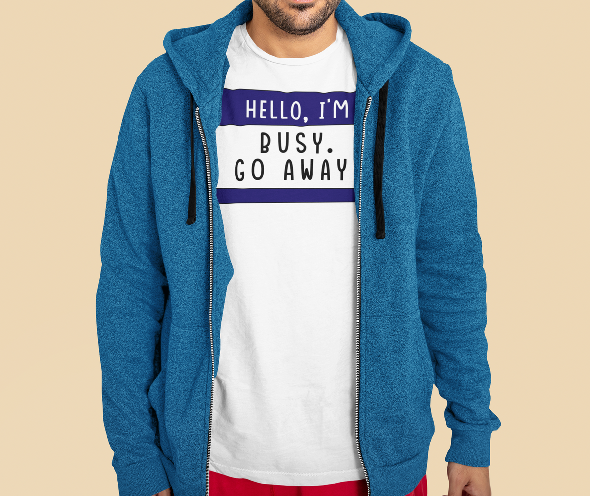 Hello I'm Busy Go Away name tag T-shirt in white, man wearing blue hoodie over it, funny introvert tee