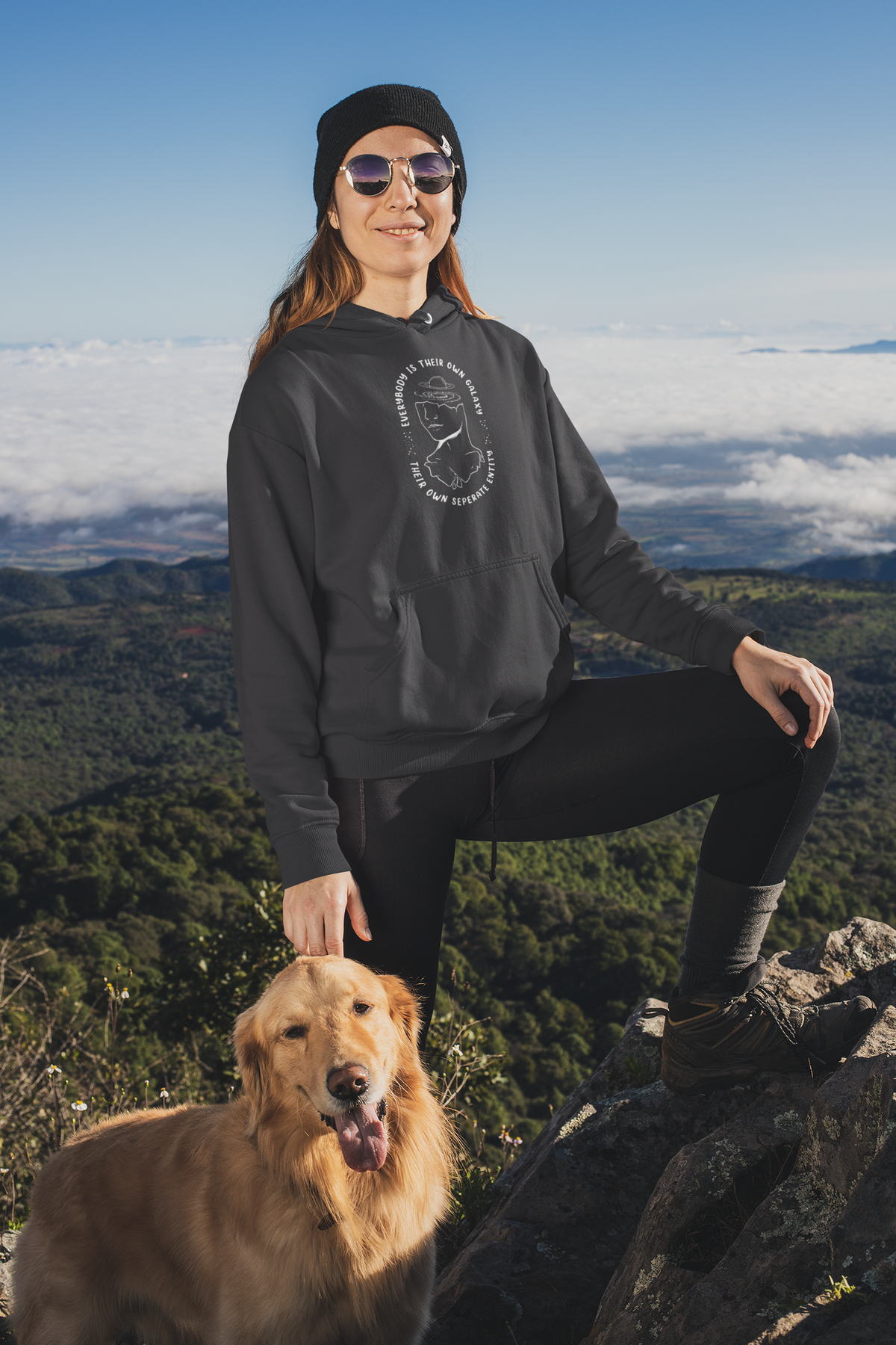 'Everybody Is Their Own Galaxy' illustrated hoodie in black, woman wearing it hiking with her dog, cozy gift