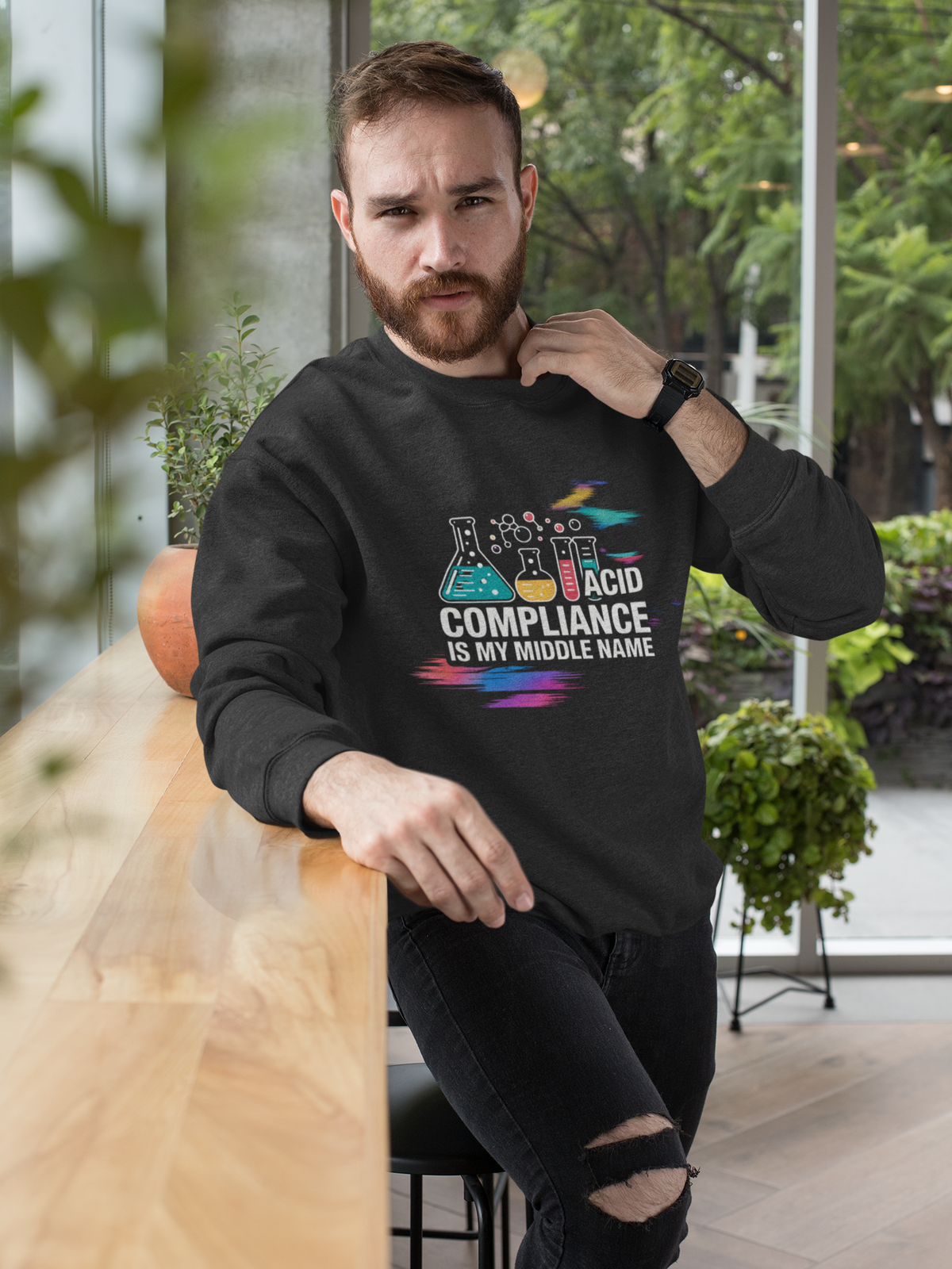 'ACID Compliance Is My Middle Name' sweatshirt in black, man wearing it seated among plants, funny DBA gift