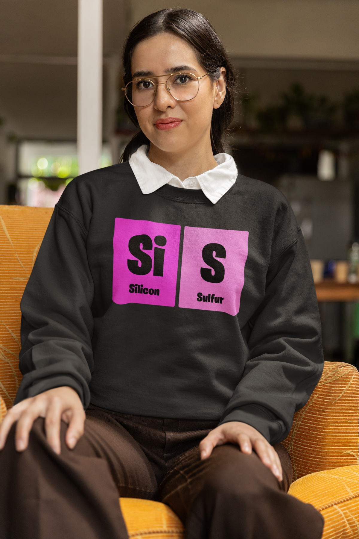 'Sis' periodic table sweatshirt in charcoal, woman sitting in an armchair wearing it, cozy photo