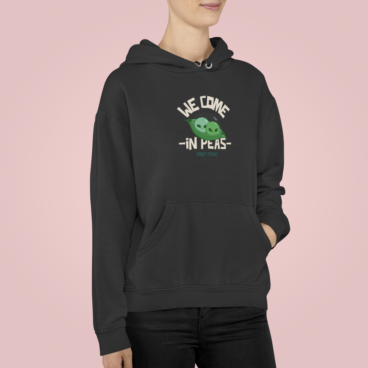 'We Come in Peas' alien pun hoodie in black, man wearing it against a pink backdrop, funny sci-fi pea gift