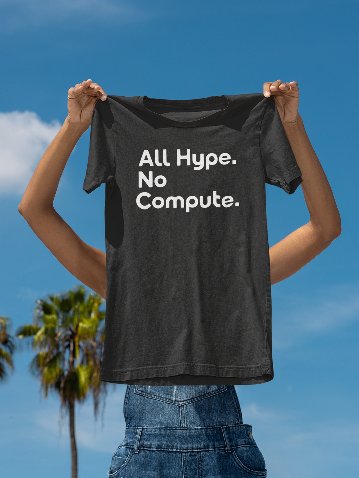 'All Hype. No Compute.' t-shirt in black, man holding it up outdoors under palm trees, funny tech gift