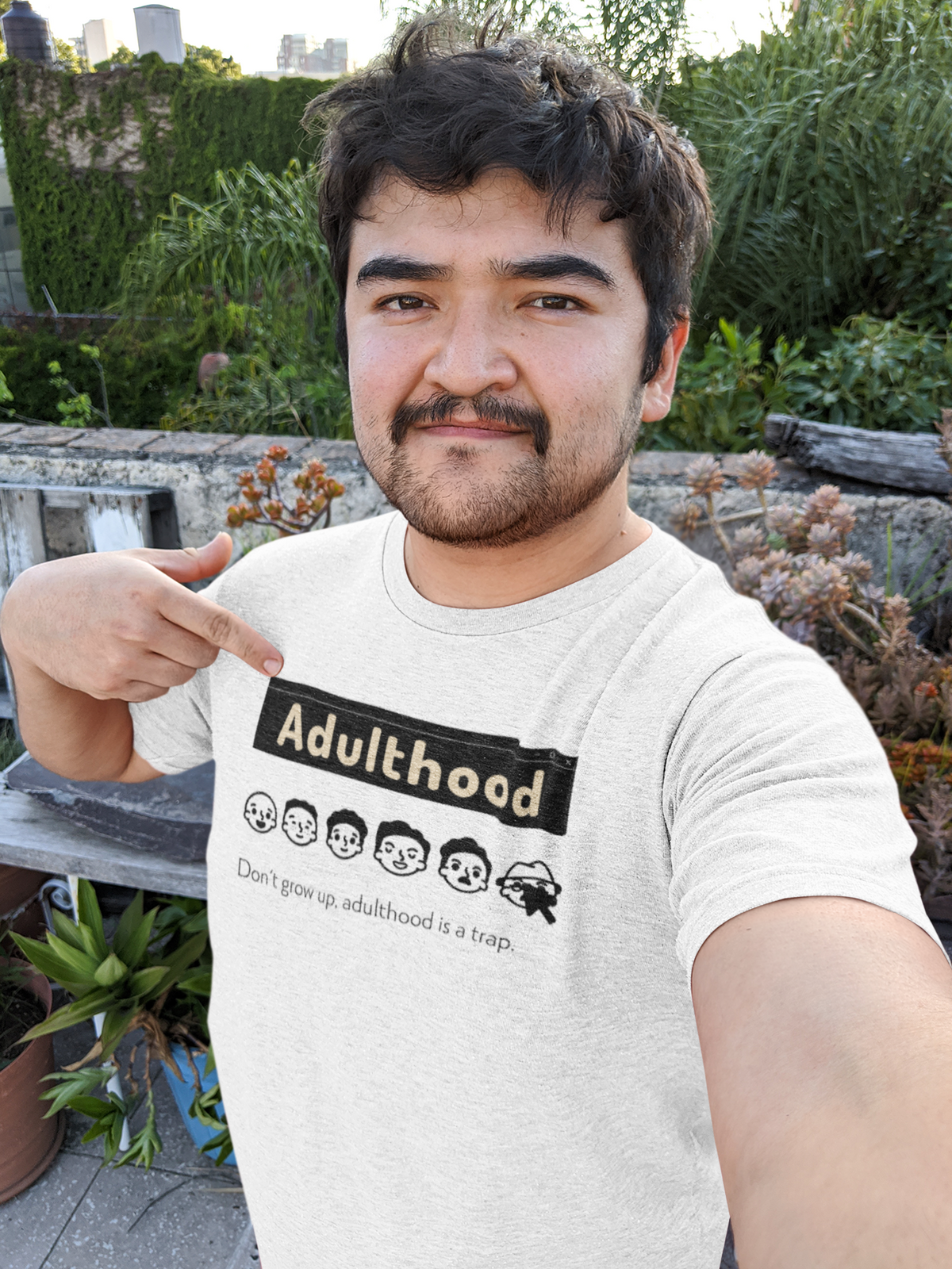 'Adulthood is a Trap' t-shirt in white, man wearing it outdoors, funny sarcastic gift for grads