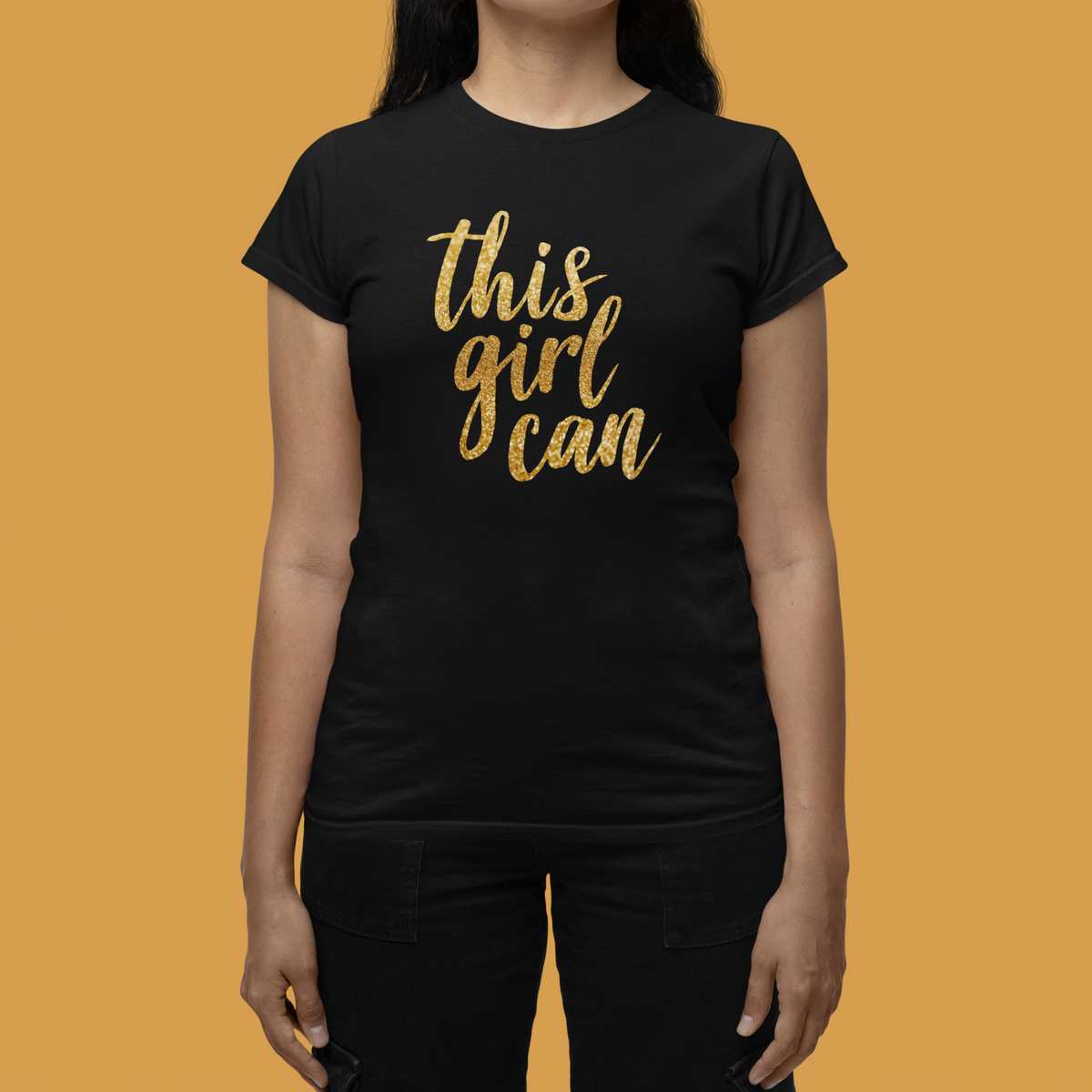 This Girl Can Women's T-Shirt in black, front flat lay against an orange backdrop, motivational gift