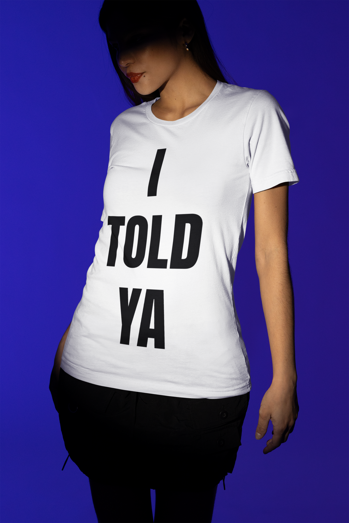 I Told Ya white t-shirt worn by a woman, cropped torso view, blue background, funny sarcastic gift