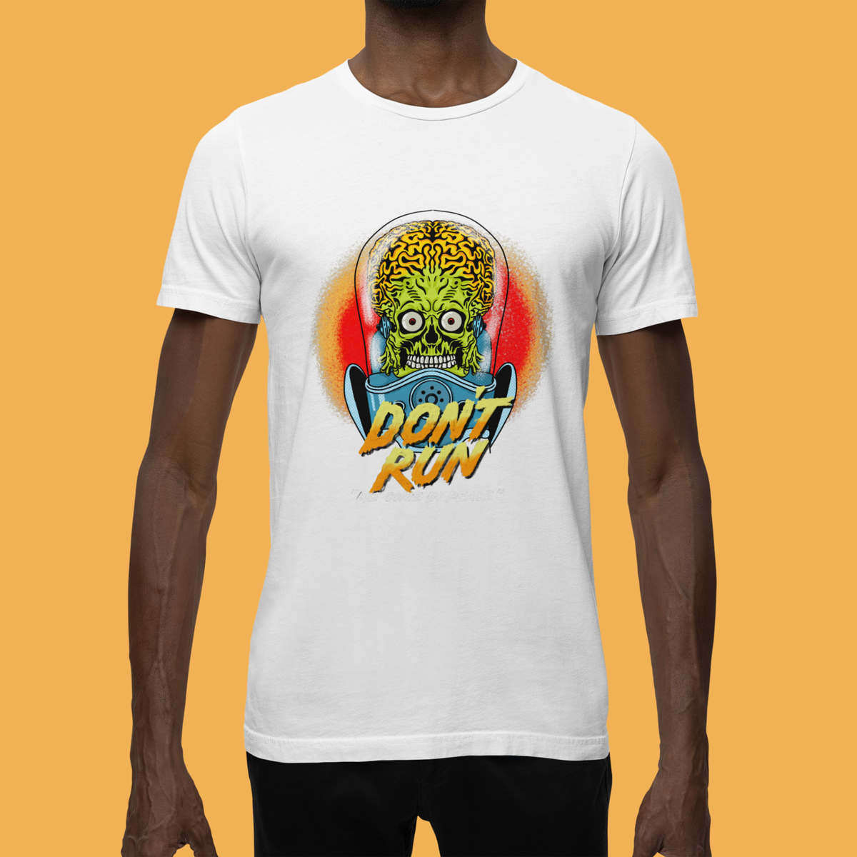 "Don't Run We Come In Peace" alien graphic t-shirt in white, man wearing it against orange background, funny sci-fi gift