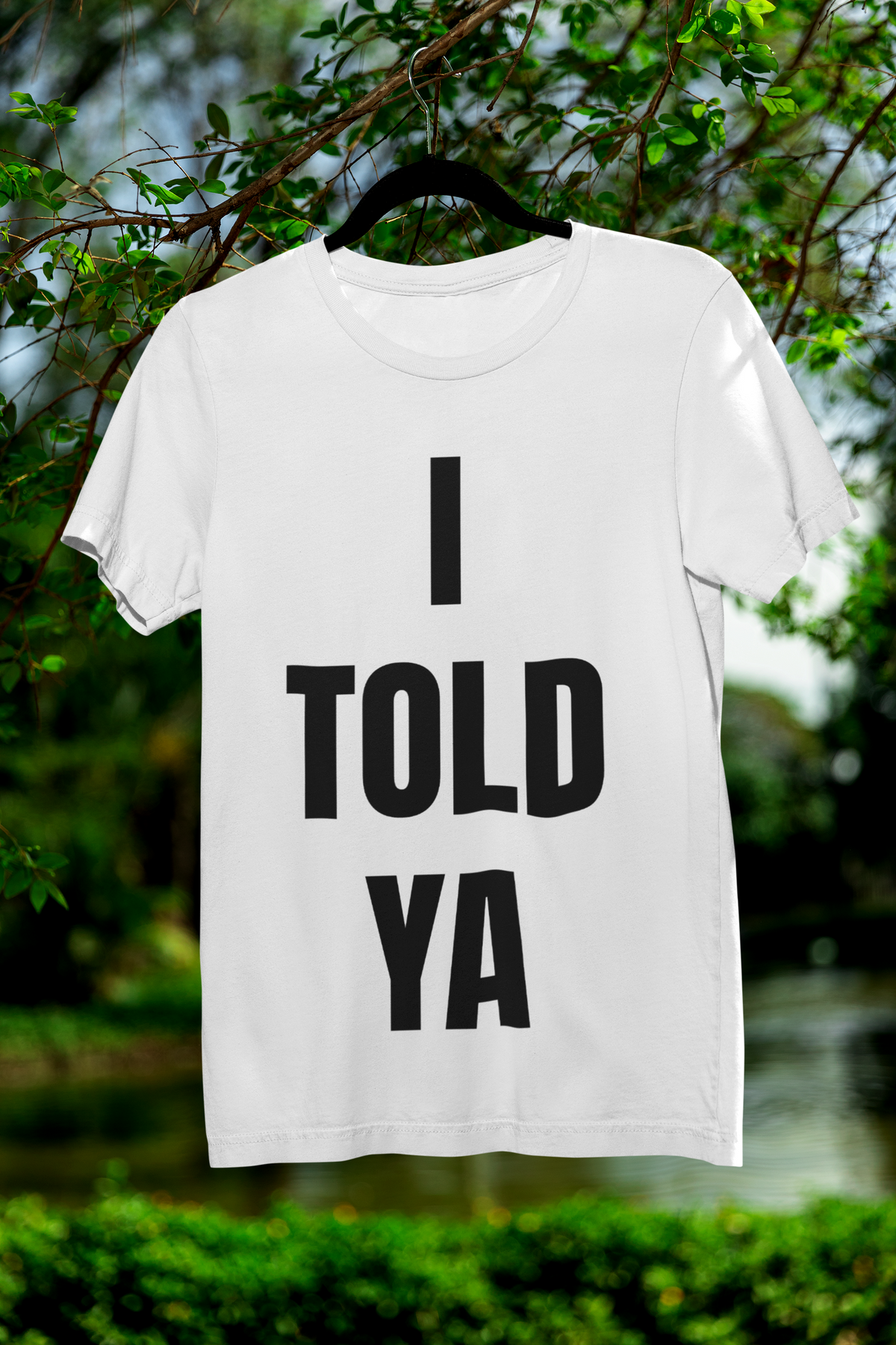 I Told Ya white t-shirt hanging outdoors on a hanger among trees, funny sarcastic gift idea