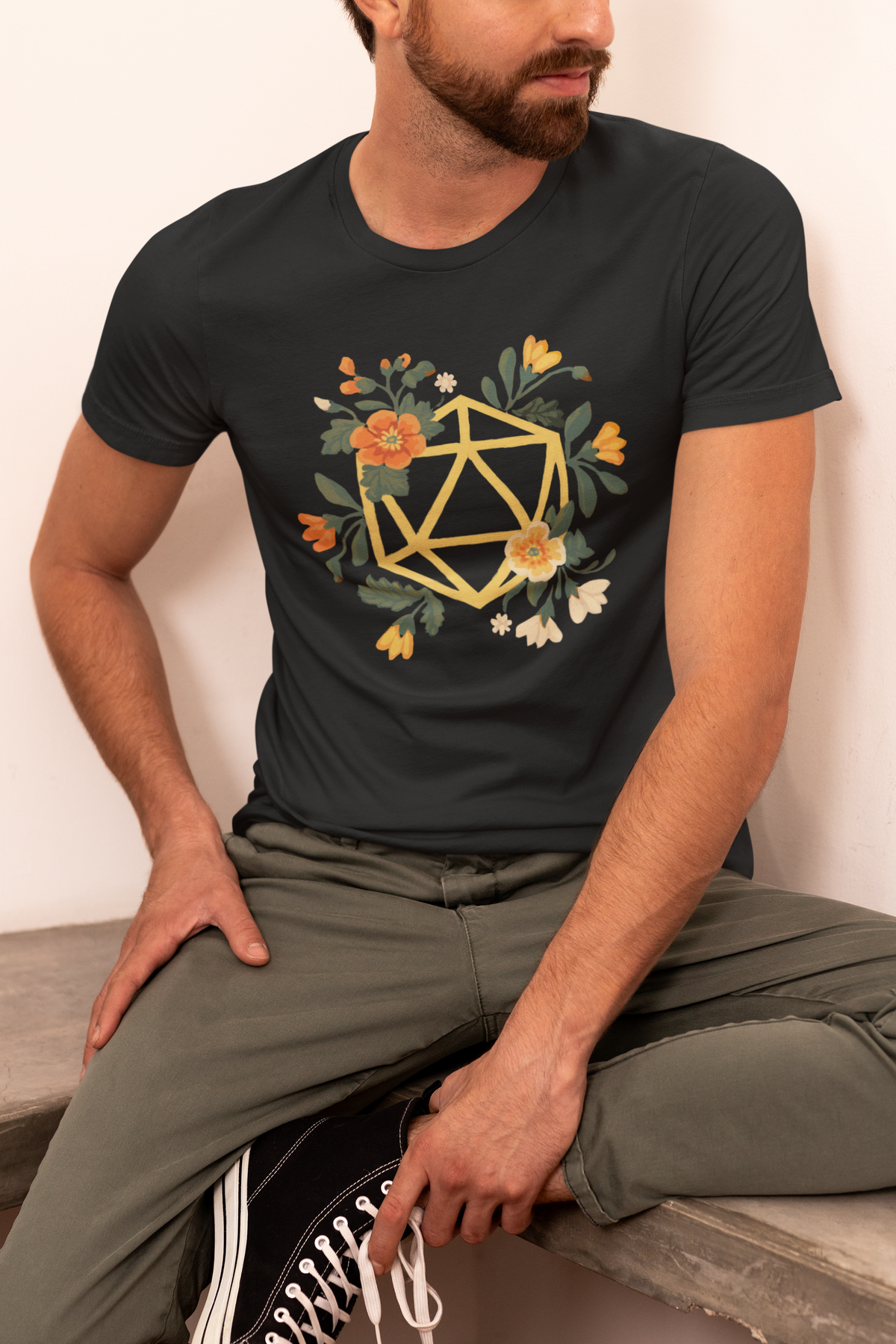 Flower Polyhedron T-Shirt in black, seated man wearing it, floral d20 print gift for tabletop gamers