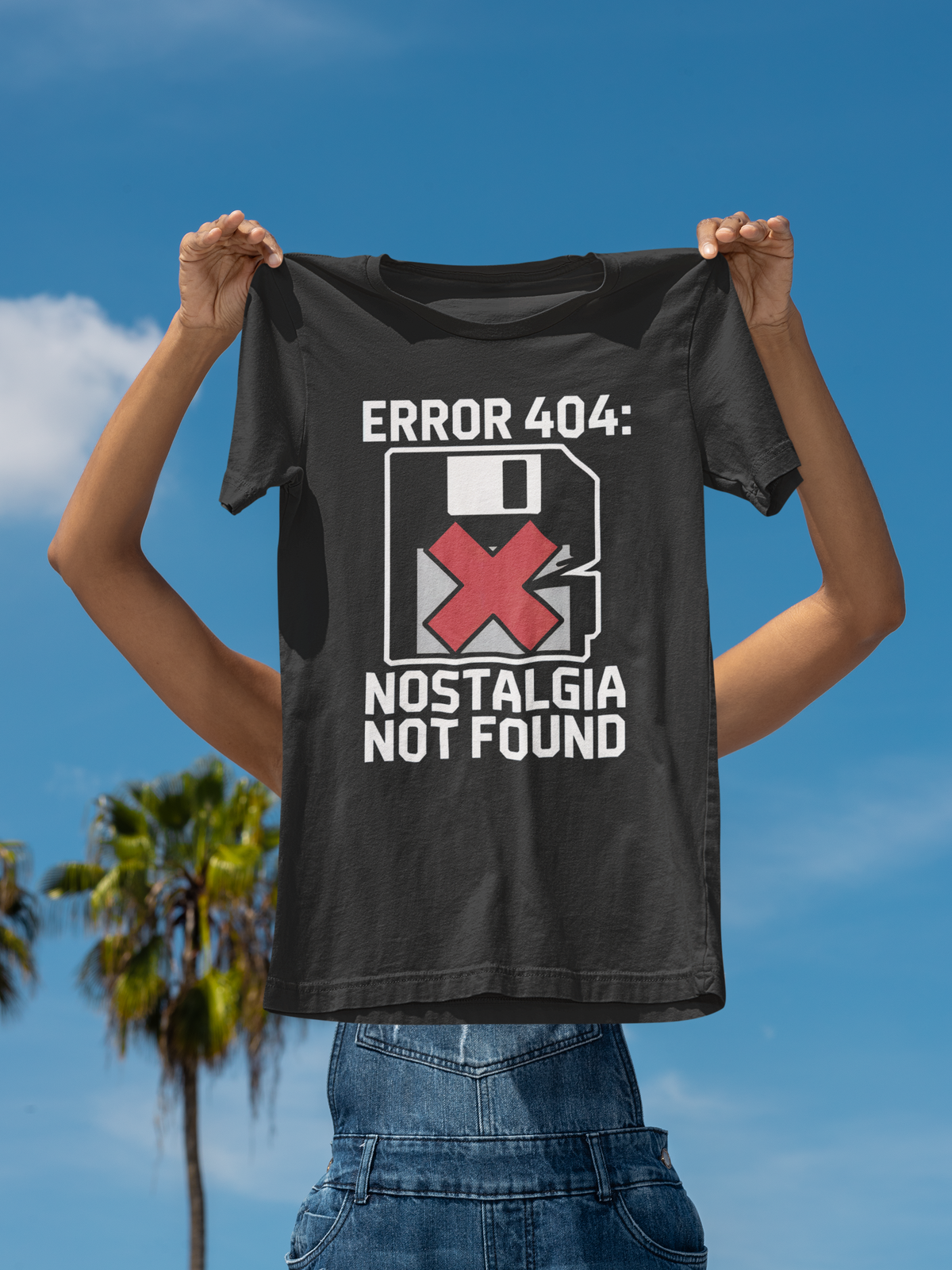 'Error 404: Nostalgia Not Found' tee in black, man holding it up outdoors under palm trees, funny tech gift