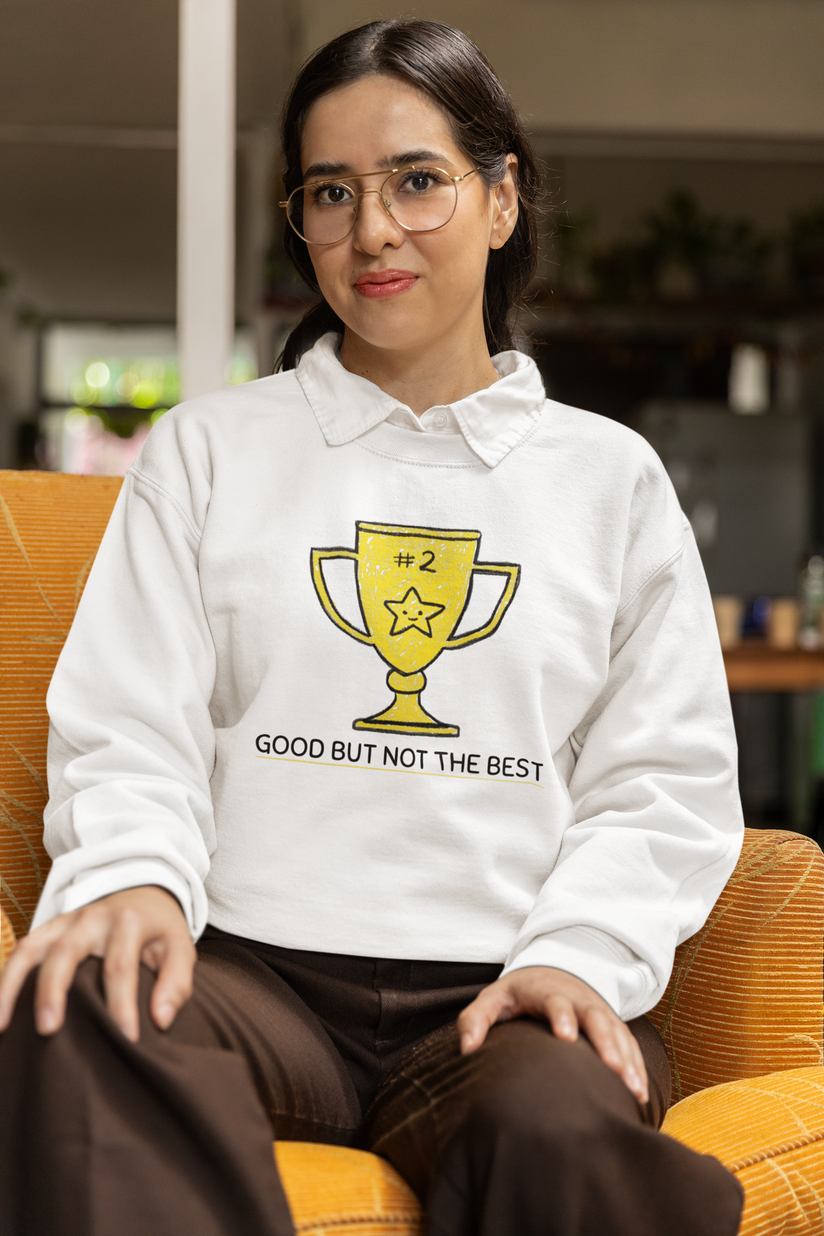 'Good But Not the Best' trophy sweatshirt in white, woman wearing it seated indoors, funny cozy gift
