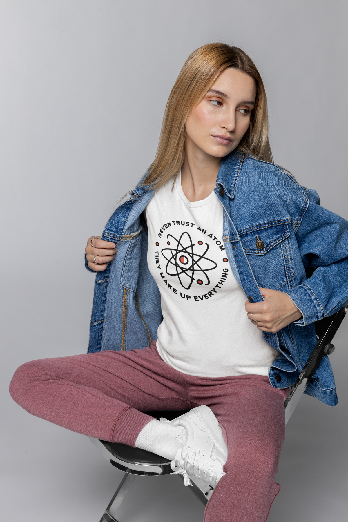 'Never Trust An Atom' t-shirt in white, woman in denim jacket wearing it, funny science gift shirt